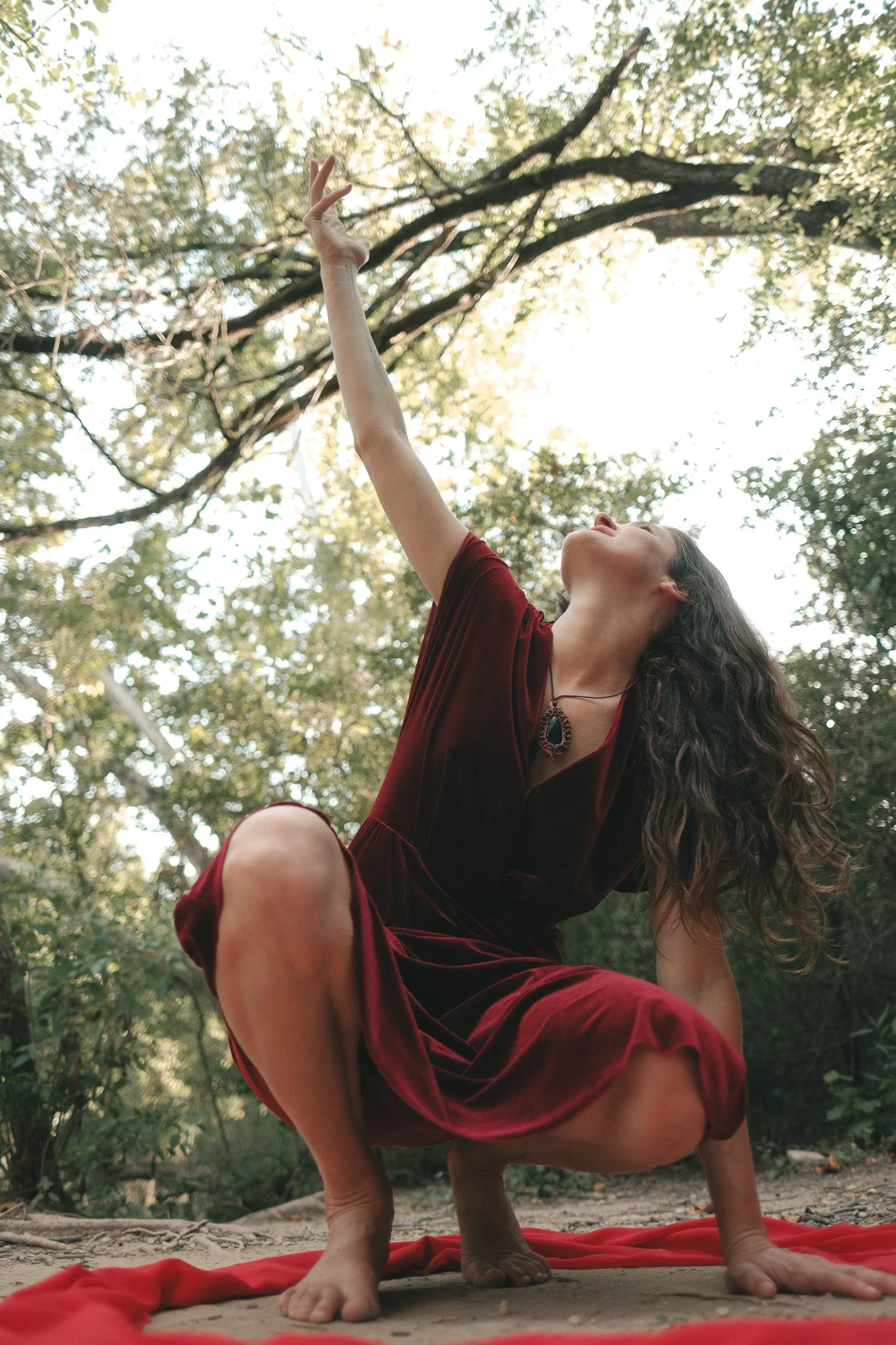 A woman inside a red circle of fabric, squatting with one hand on the ground and the other reaching up to the sky.