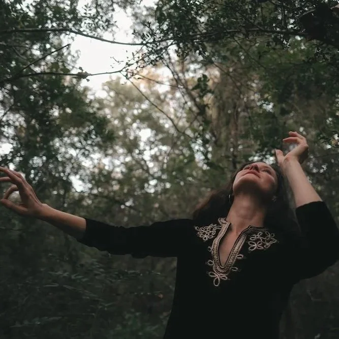 Woman with arms raised and head tilted back in a forest during daytime.