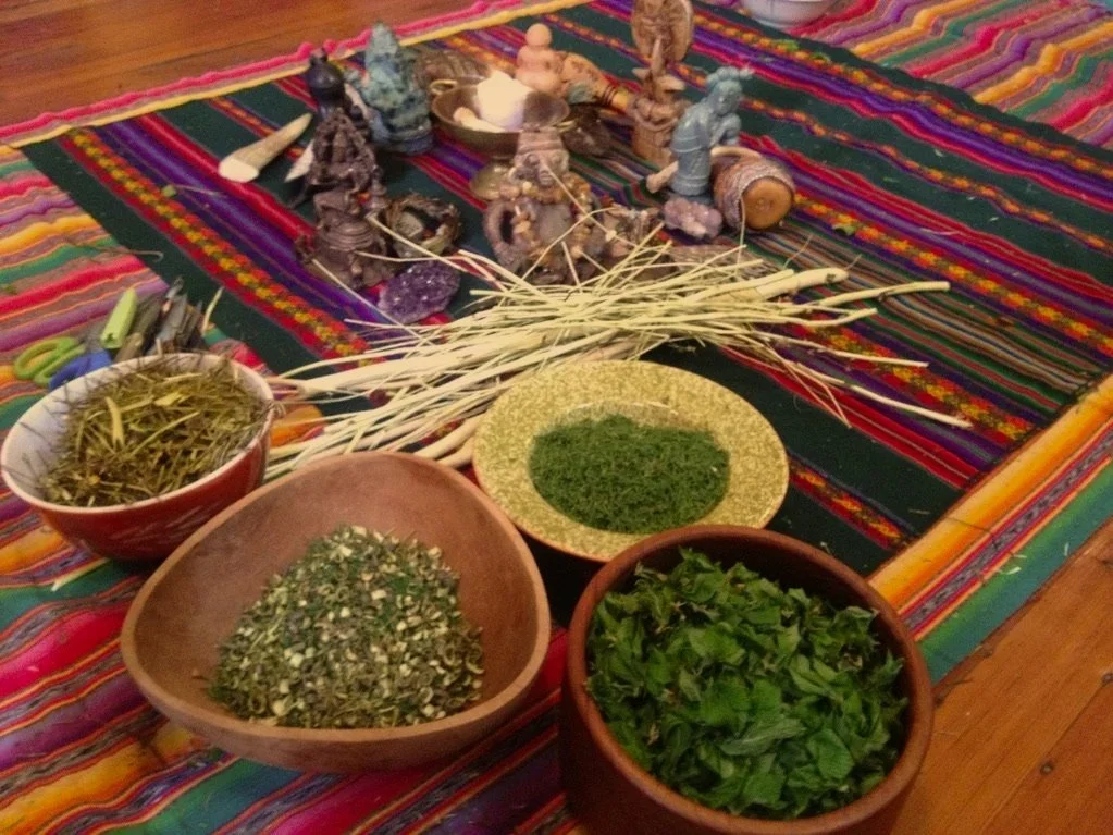 A colorful tablecloth with various herbs, dried plants, and small statues of deities arranged on it.