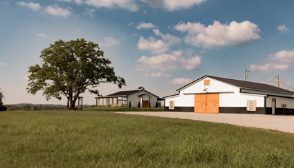 Farm buildings with a large tree in a grassy field under a partly cloudy sky.