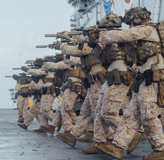 Military soldiers in camouflage uniforms and gear aiming rifles during a training exercise on a ship.