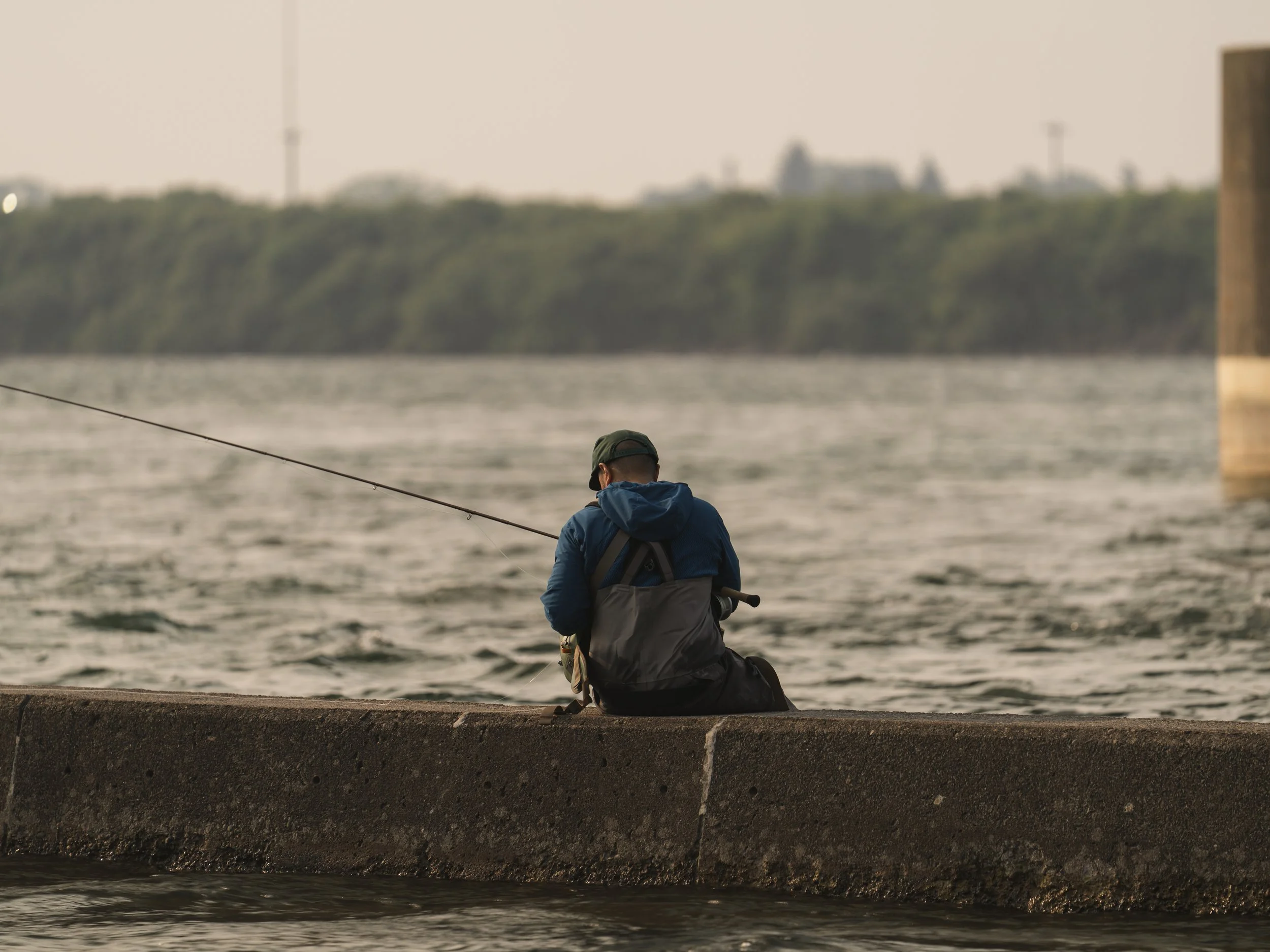 Angler sitting on a burm at dawn, a distant city skyline across the water