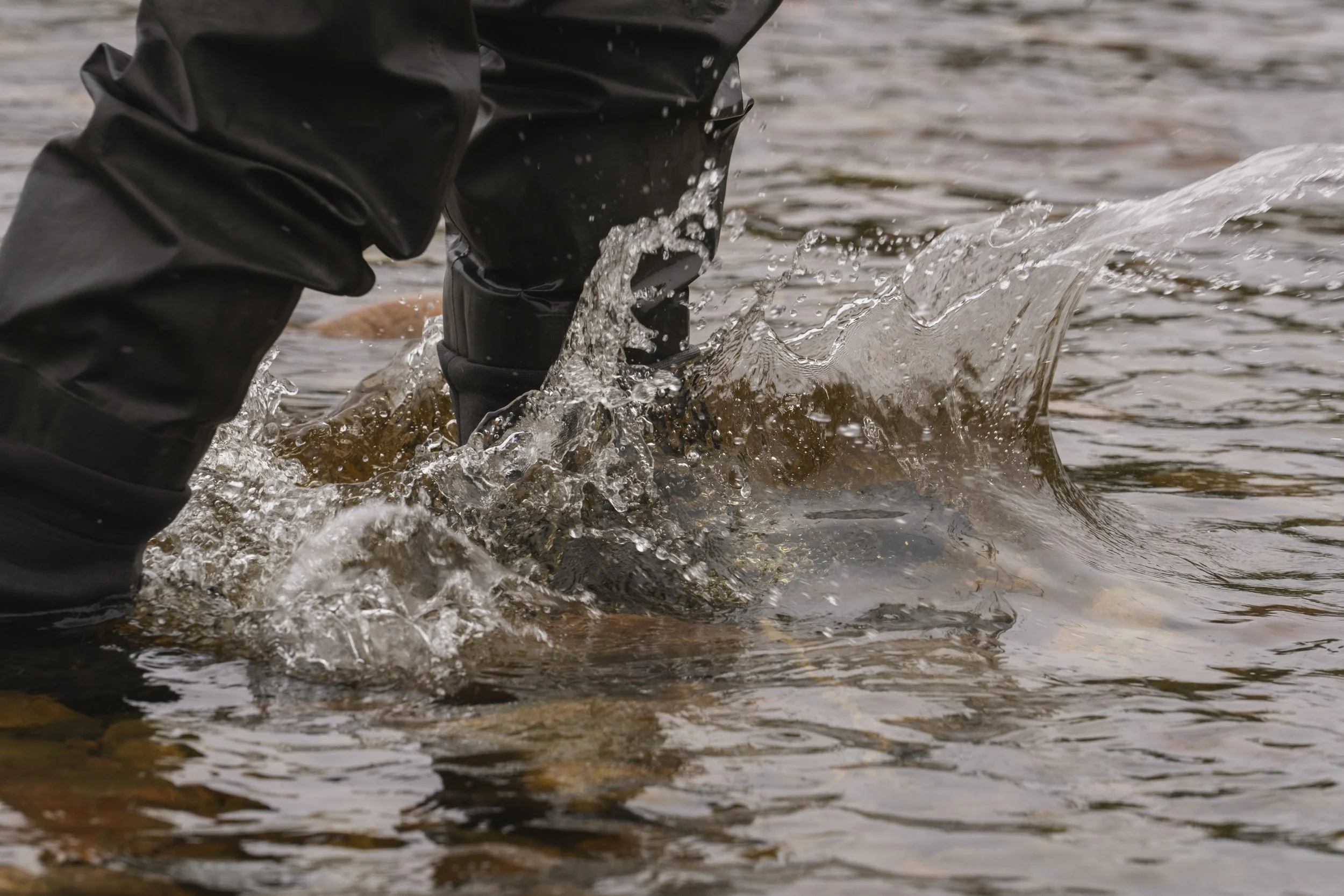 Close-up of waders splashing through moving river water