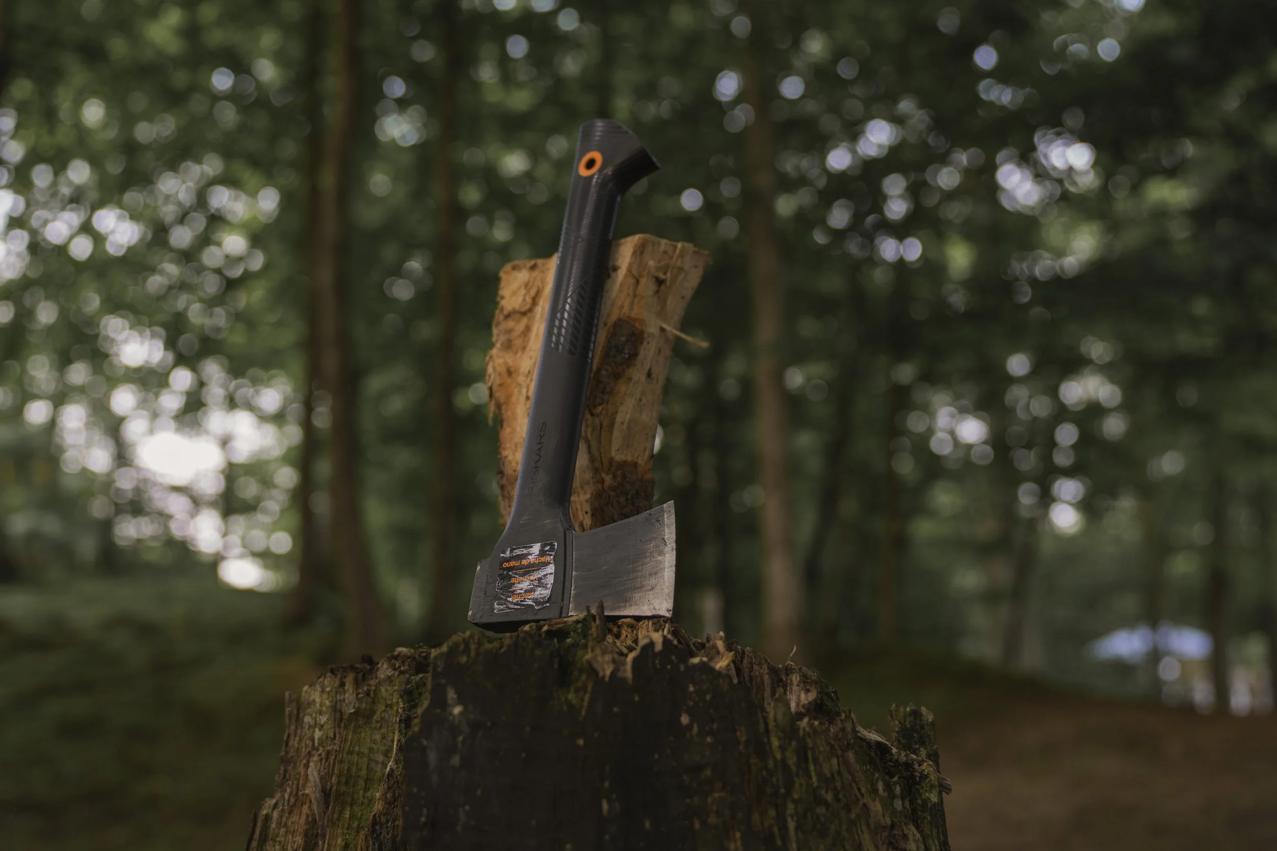 Fiskar's hatchet with orange detailing sitting next to a split log atop a weathered tree-stump chopping block