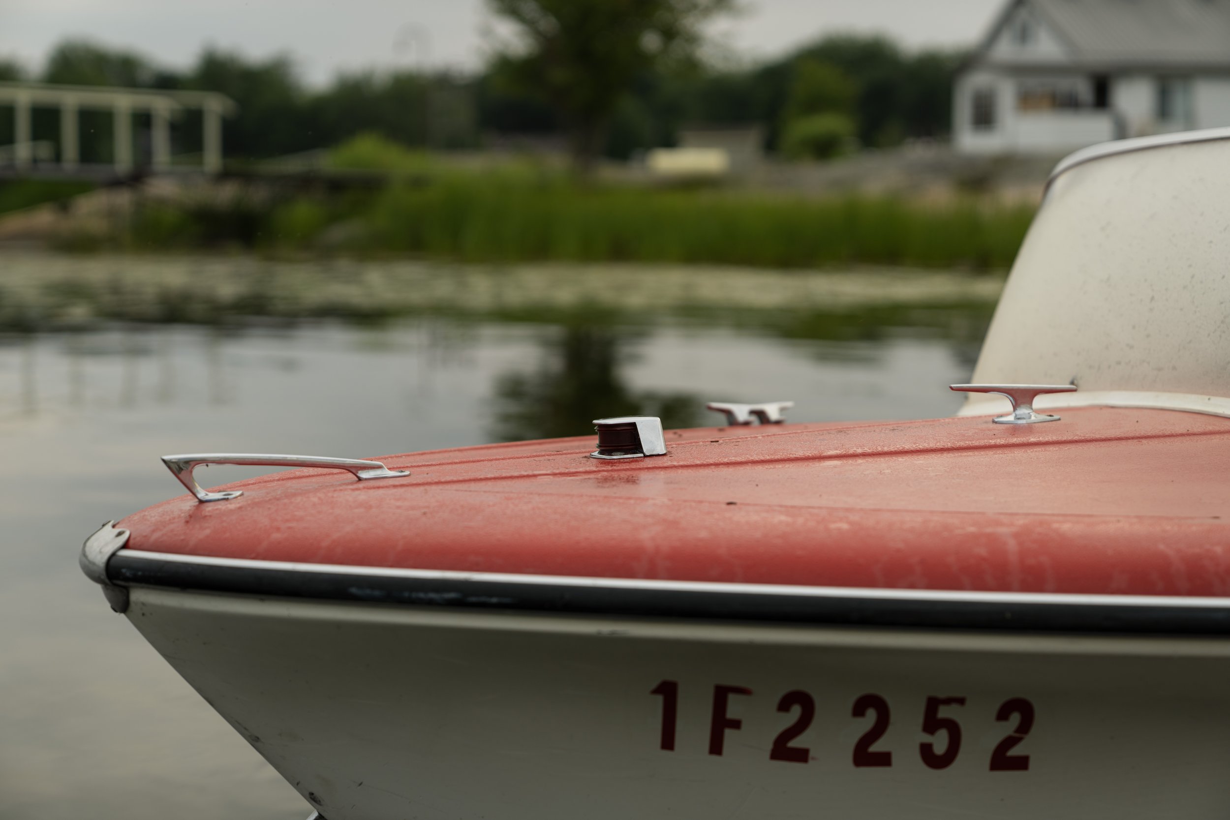 Chrome bow hardware and cleats on a vintage runabout, dock and cottage soft behind