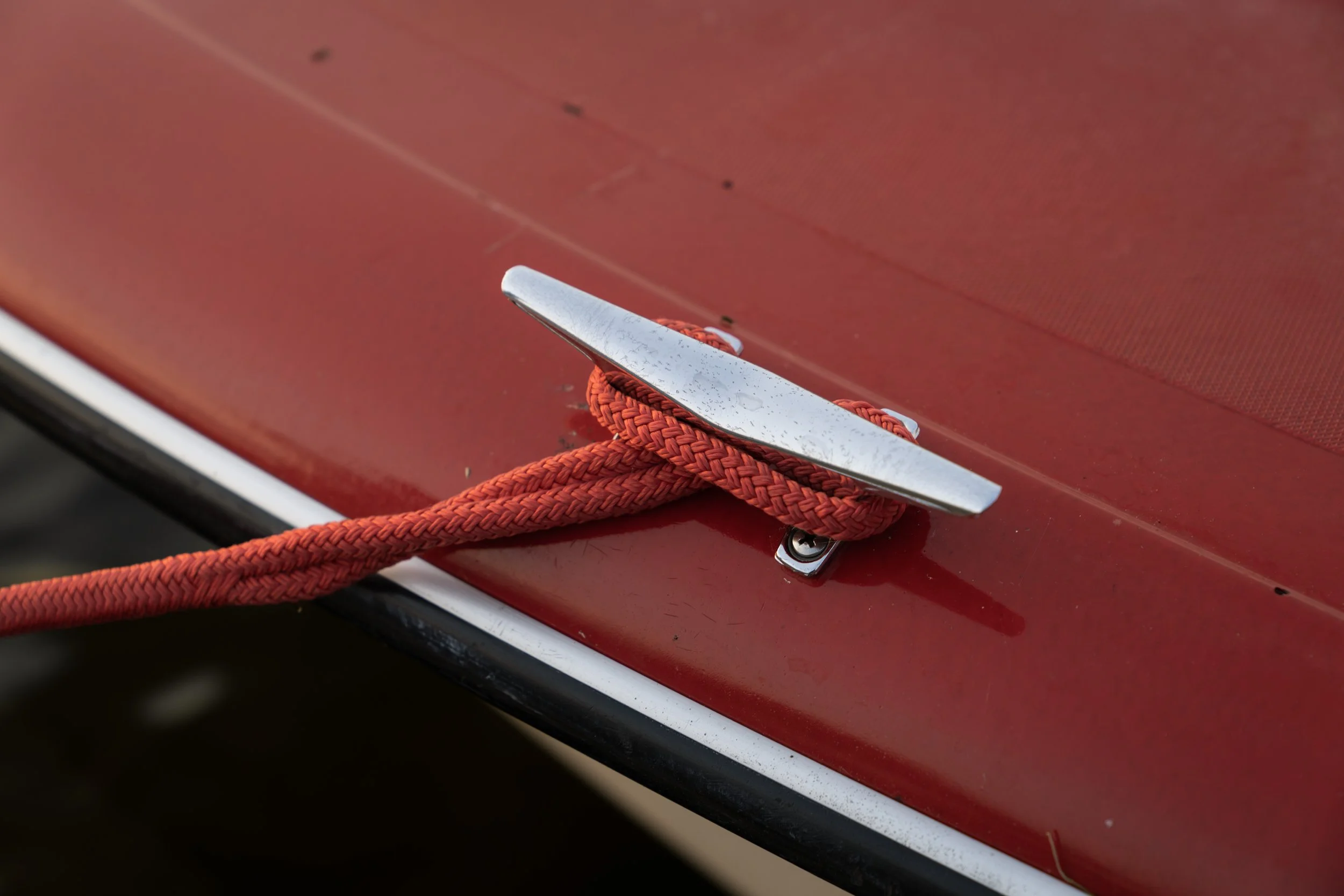 Red mooring line hitched to a chrome cleat on a red boat hull