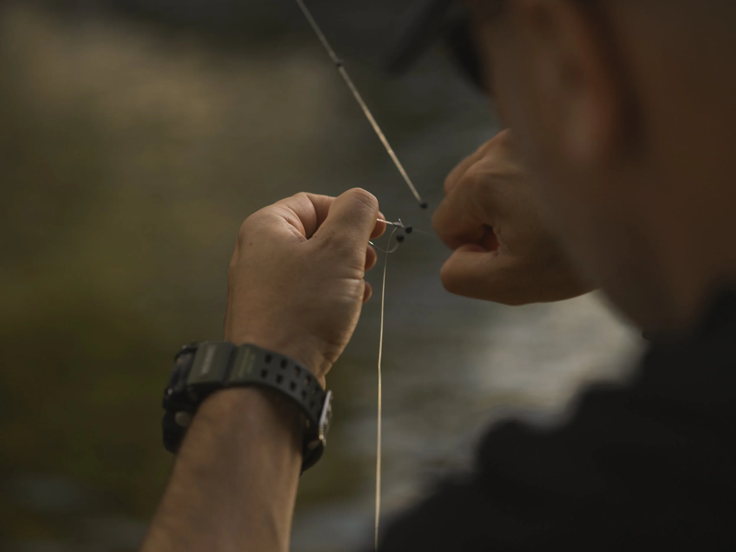Close-up of an angler's hands rigging his line at the water's edge