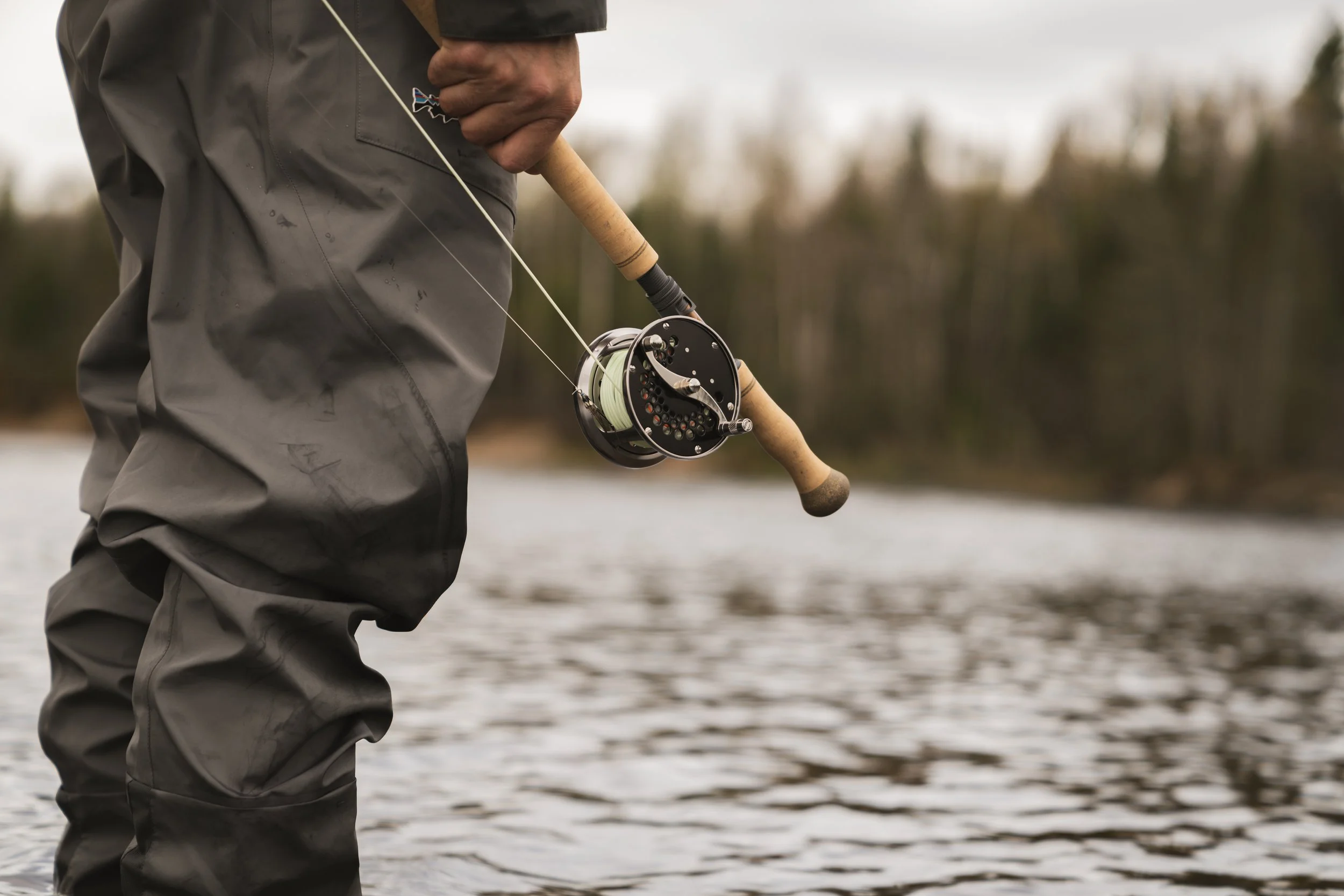 Angler in Patagonia waders holding a Sage R8 and Loop classic reel while standing in the river