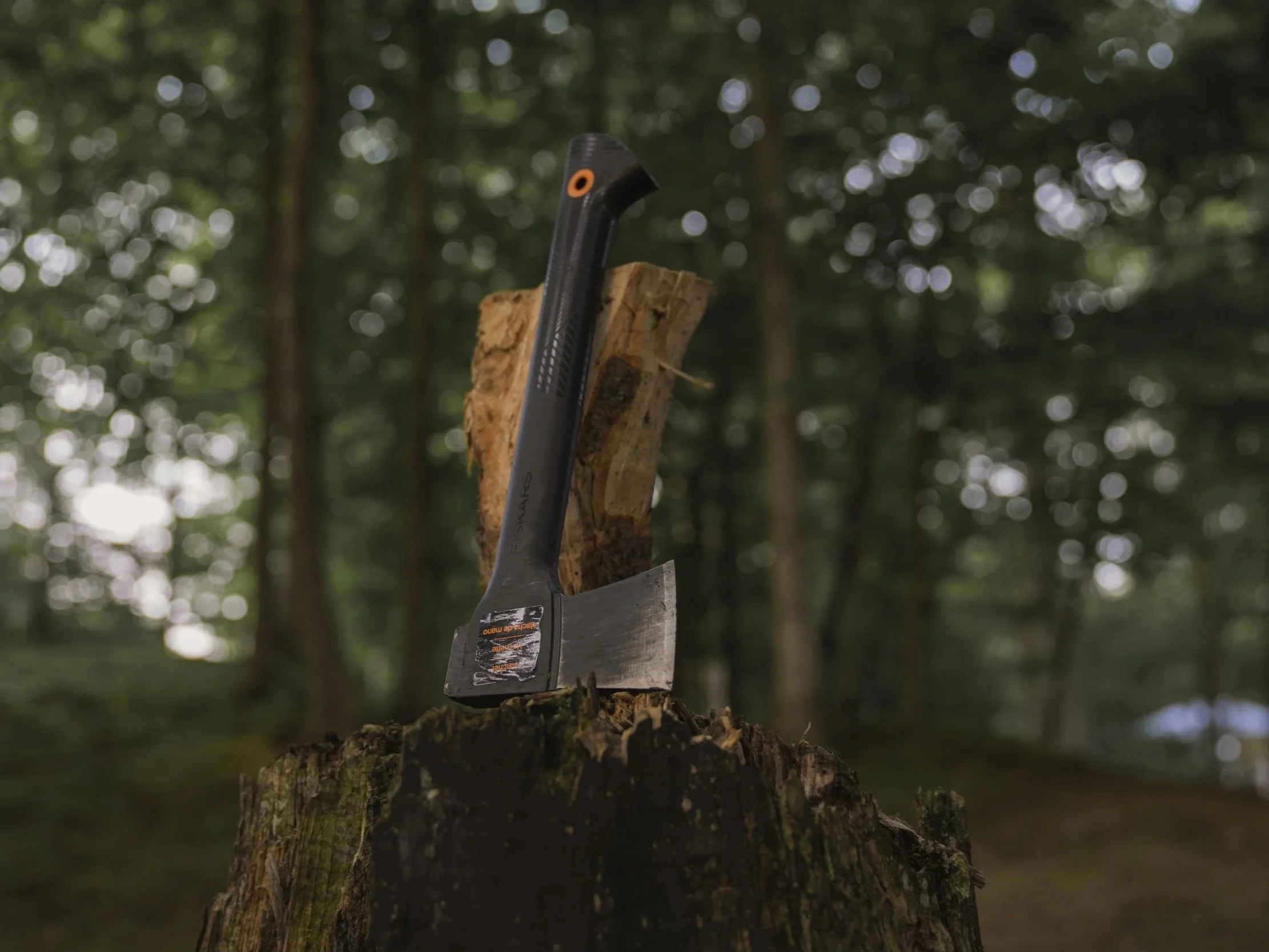 Fiskar's hatchet with orange detailing sitting next to a split log atop a weathered tree-stump chopping block