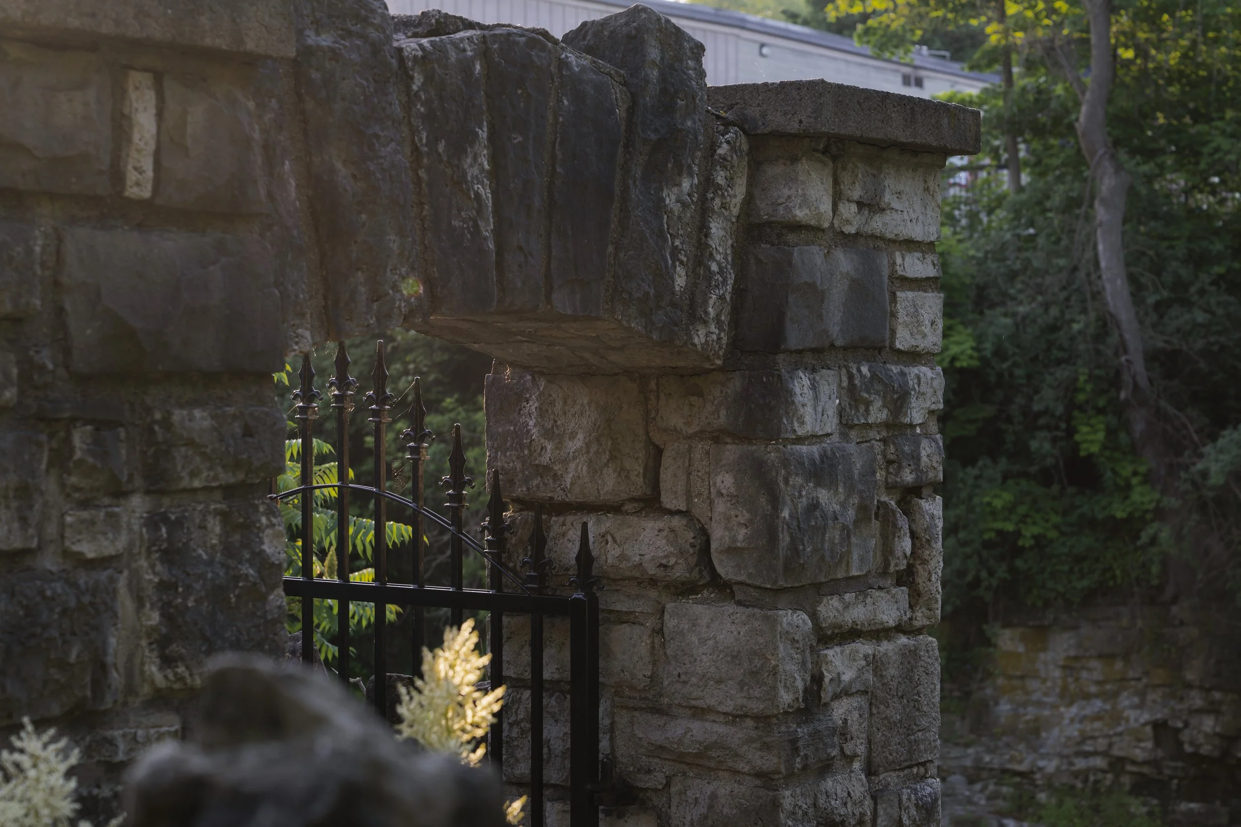 Weathered stone pillars and an iron gate beside large rock slabs in the trees