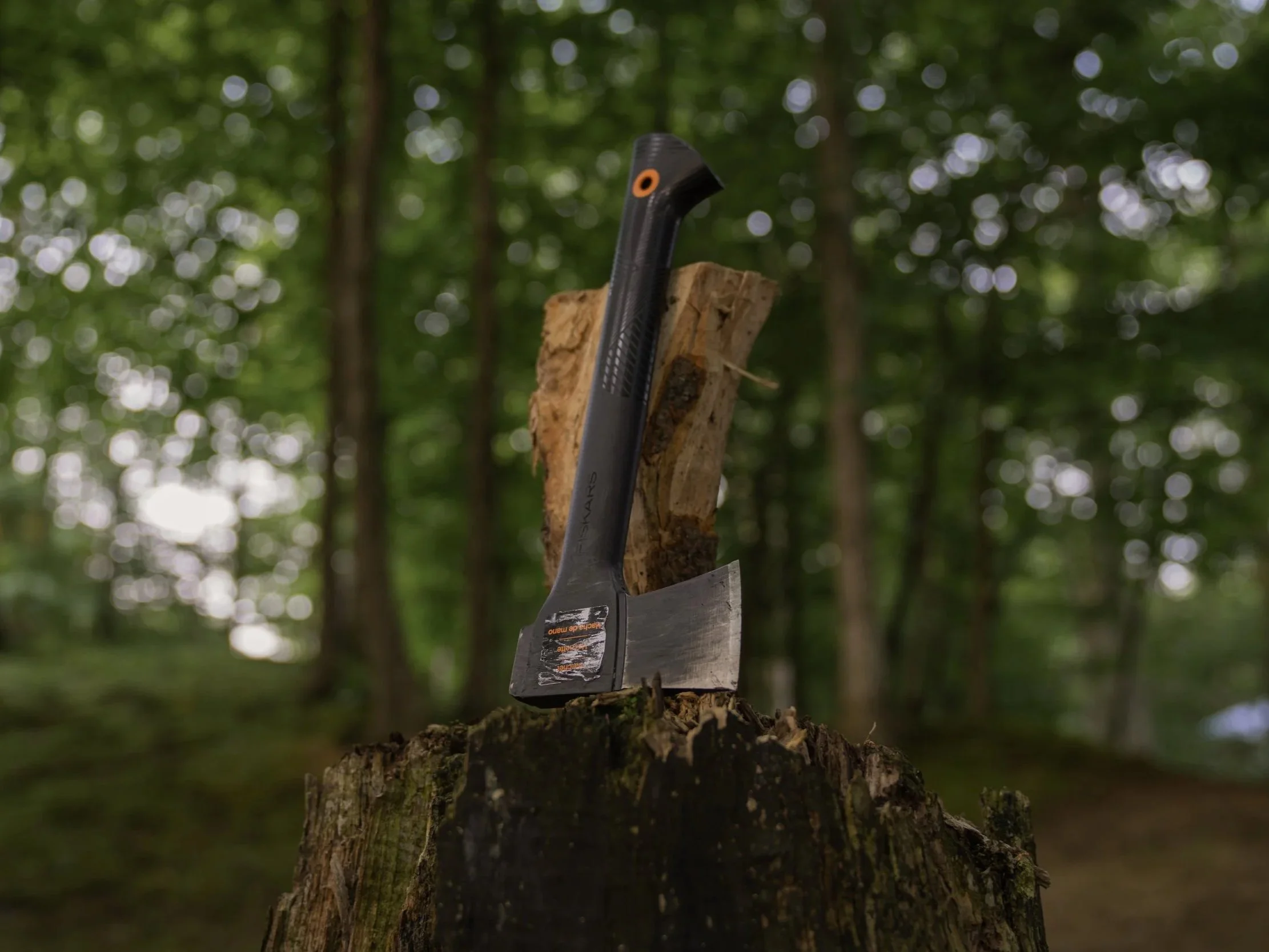 Fiskar's hatchet with orange detailing sitting next to a split log atop a weathered tree-stump chopping block