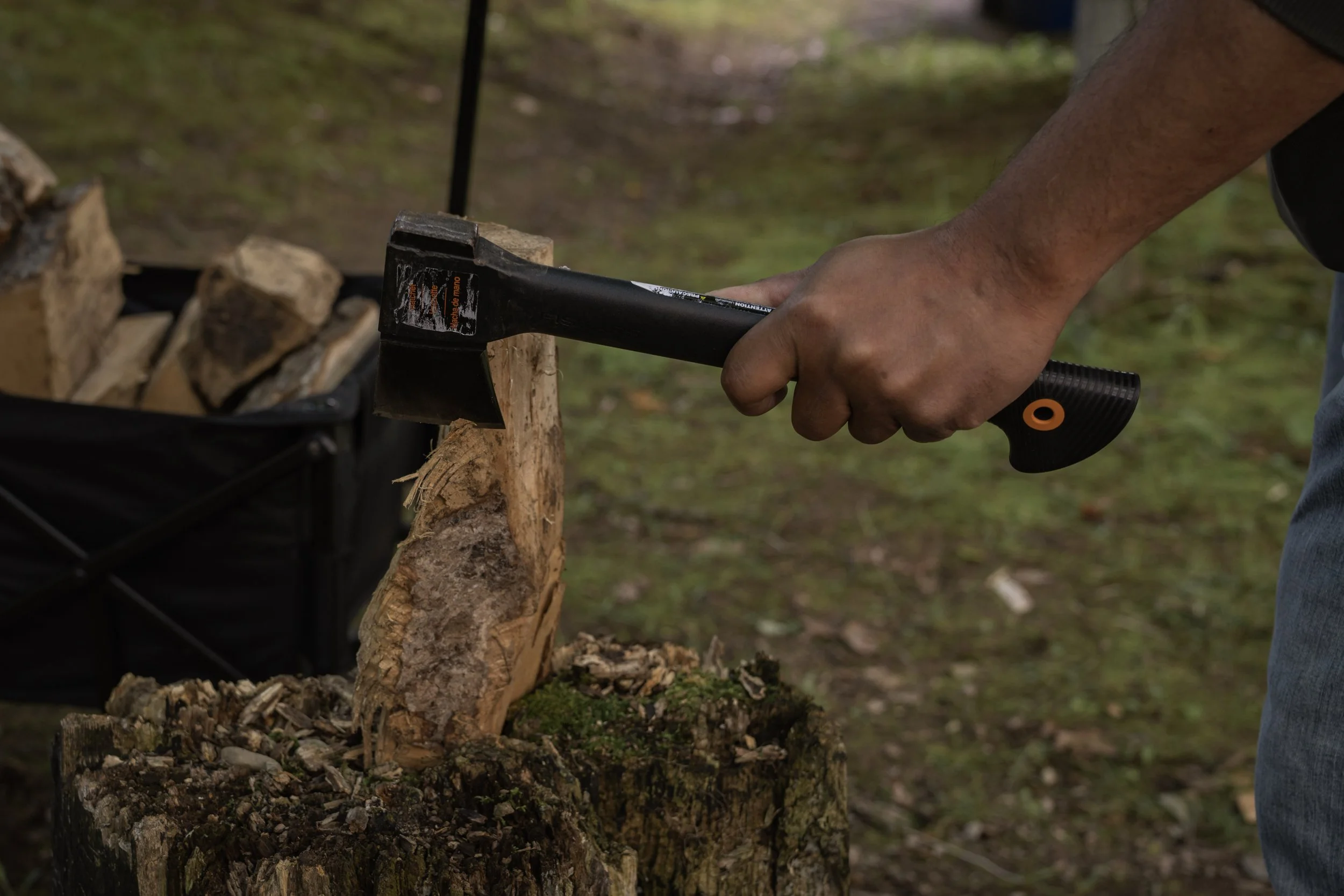 Man splitting firewood with a Fiskar's hatchet on a stump, a crate of split logs behind