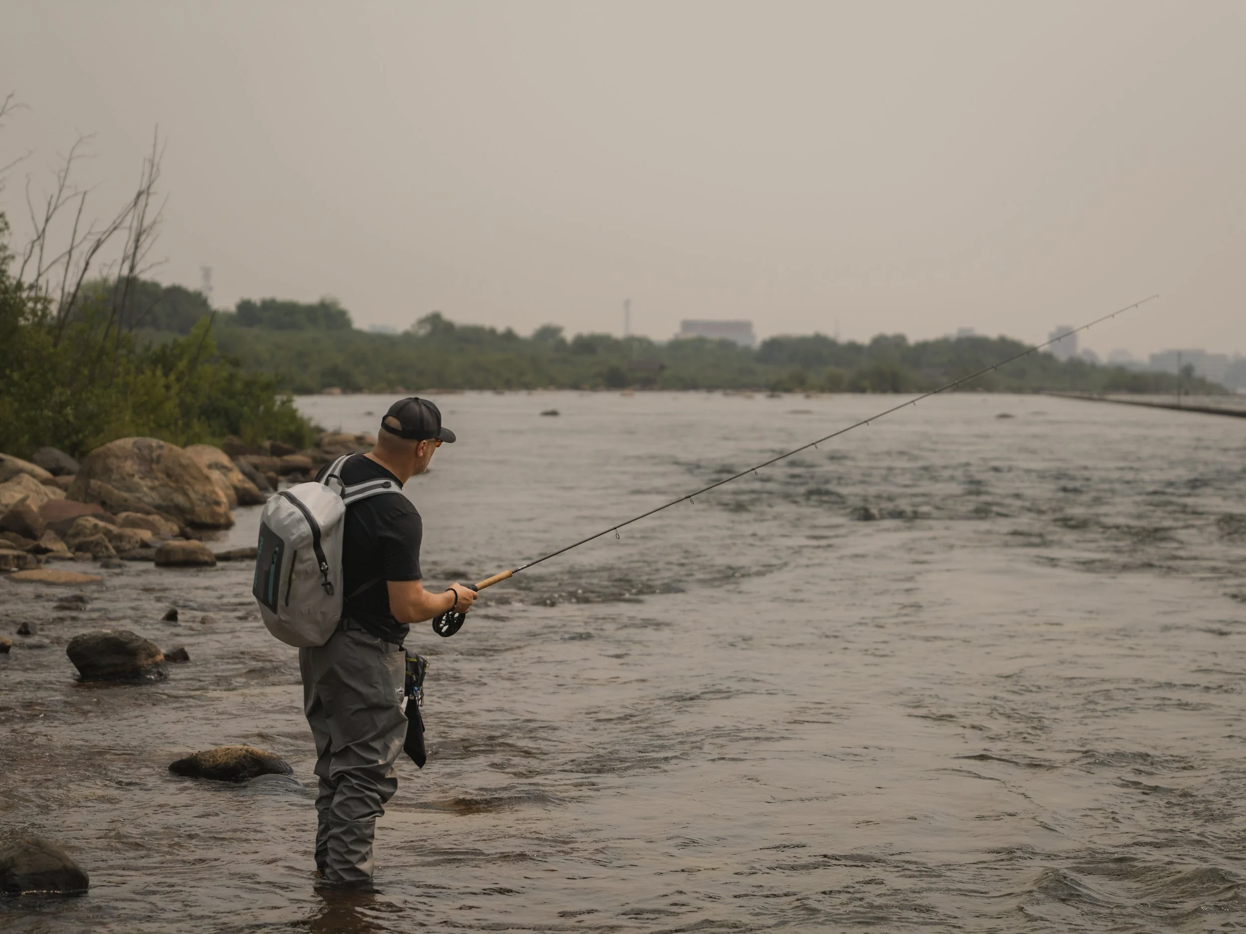 Angler with a  Patagonia backpack casting from a rocky riverbank into hazy open water