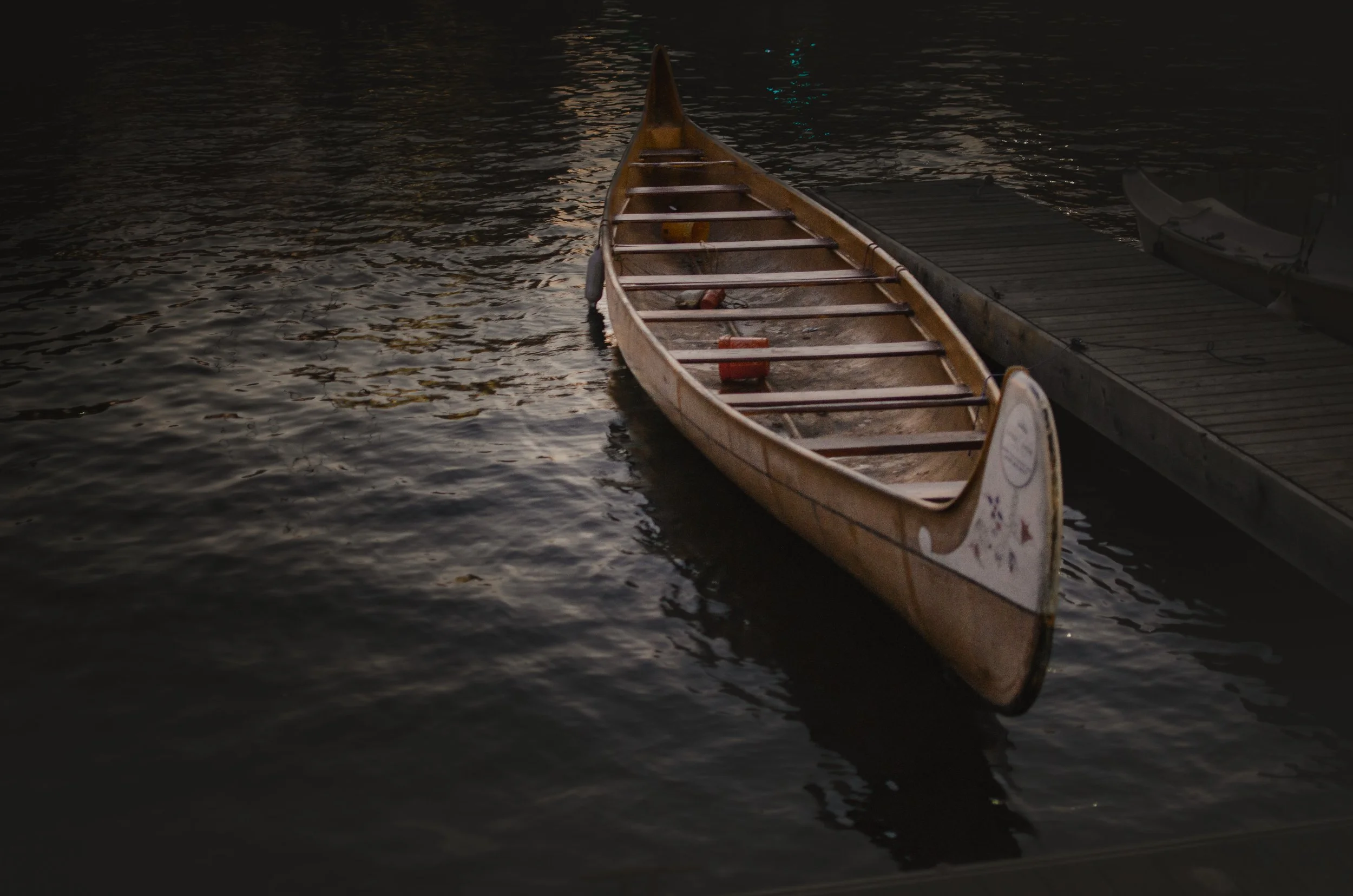 Wooden cedar-strip canoe moored beside a dock on still, dark water at dusk