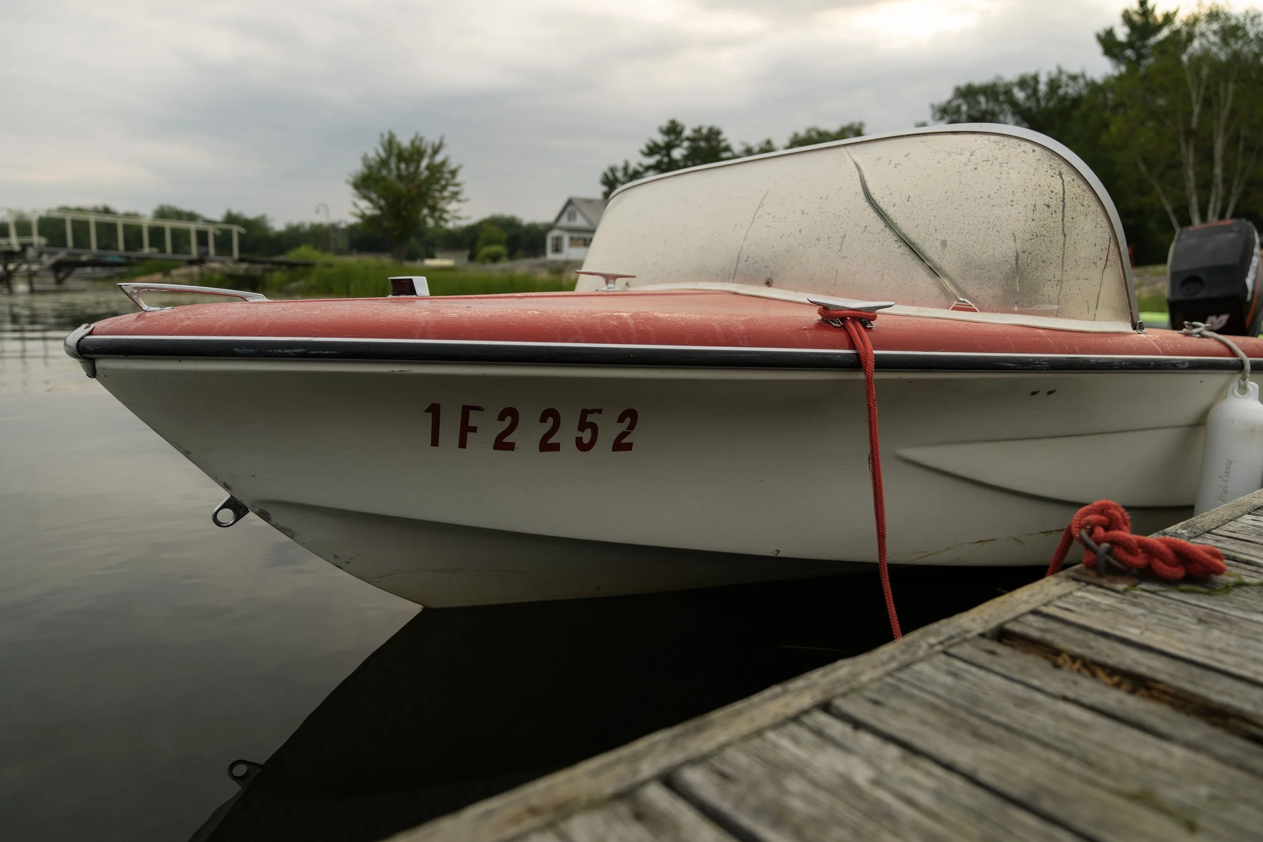 Vintage red-and-white runabout moored at a wooden dock, cottage behind, overcast morning