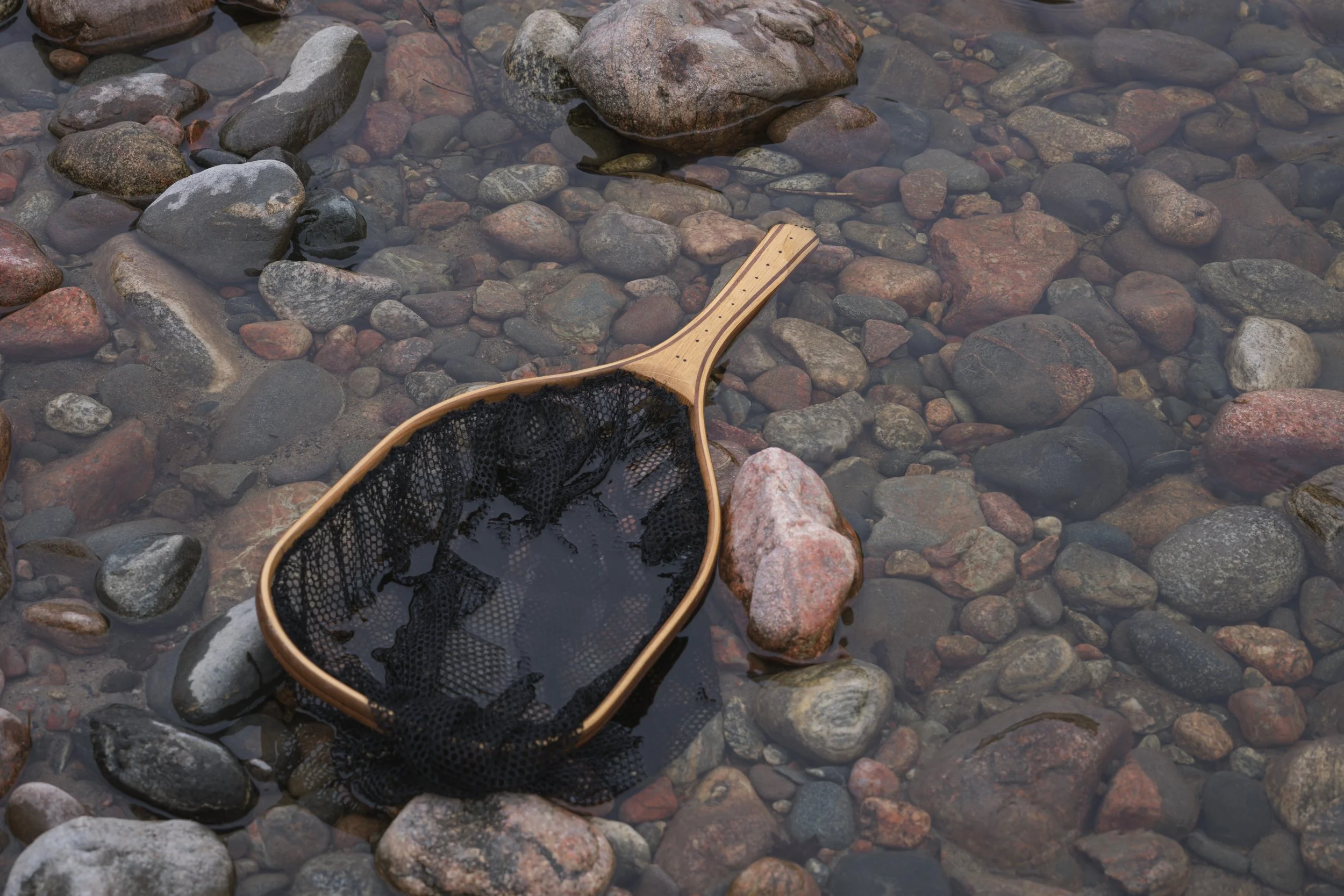 Wooden Cedar landing net resting on smooth, multicoloured river cobbles