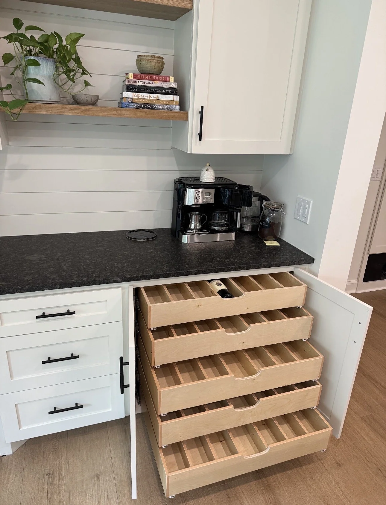 Kitchen counter with a coffee maker, jar of coffee, and wall outlet, with white and black cabinetry and open wooden drawers underneath.