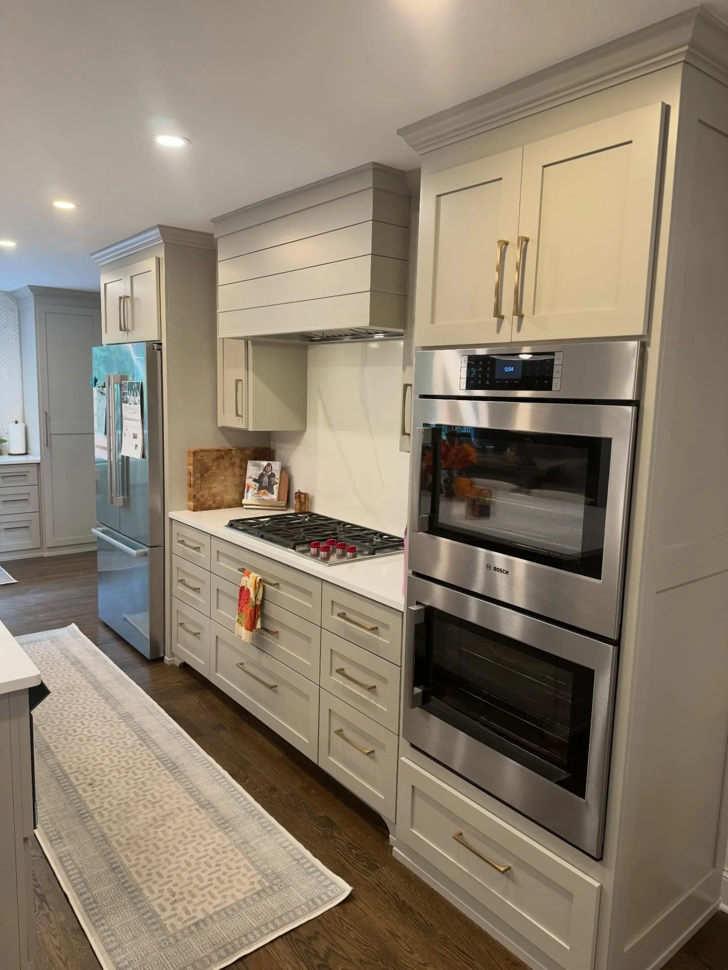 Modern kitchen with white cabinetry, stainless steel oven, built-in microwave, and refrigerator, with a beige runner rug and hardwood floors.