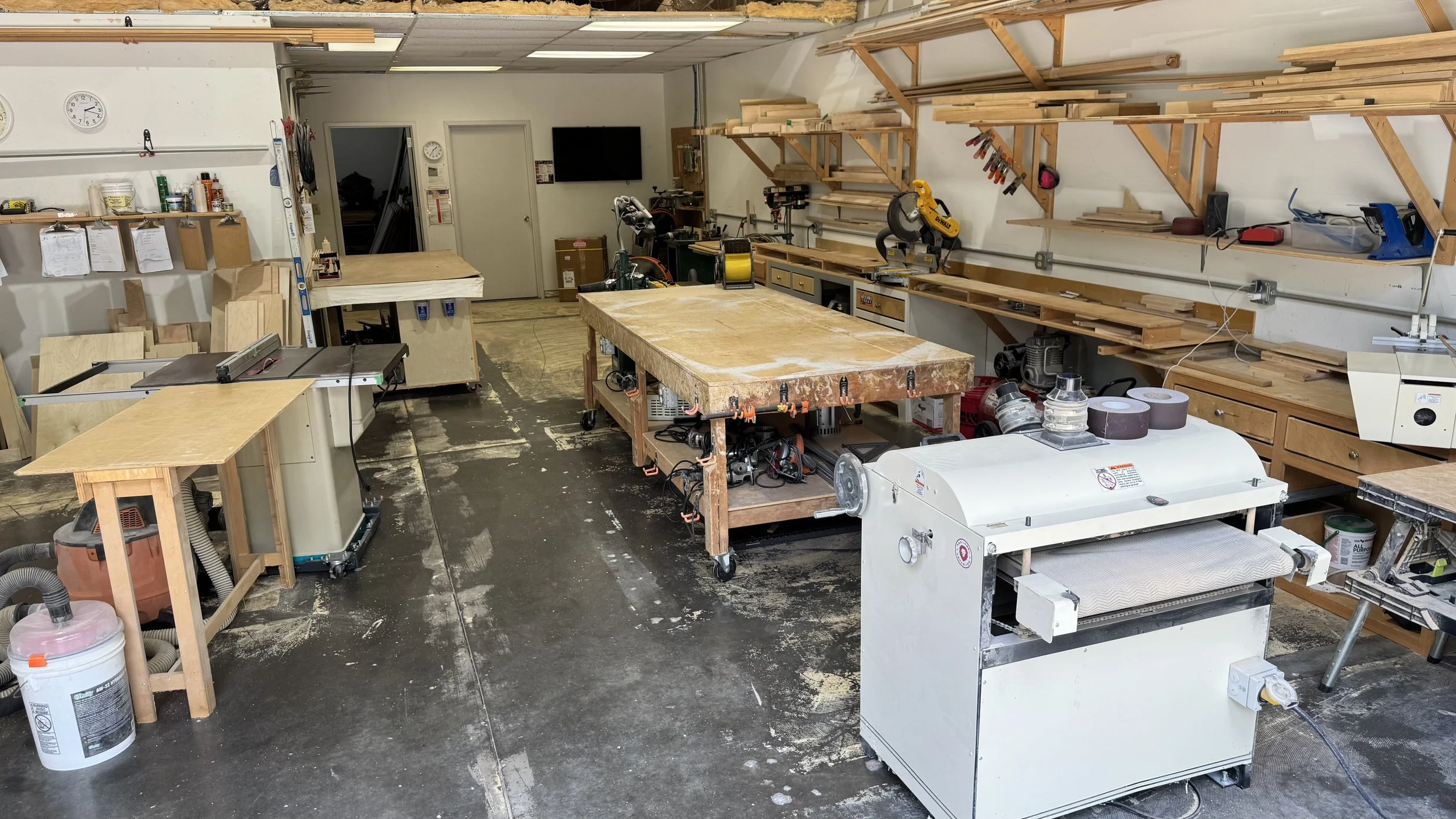 A woodworking workshop with workbenches, tools, and wooden planks, along with a vacuum and woodworking machinery.