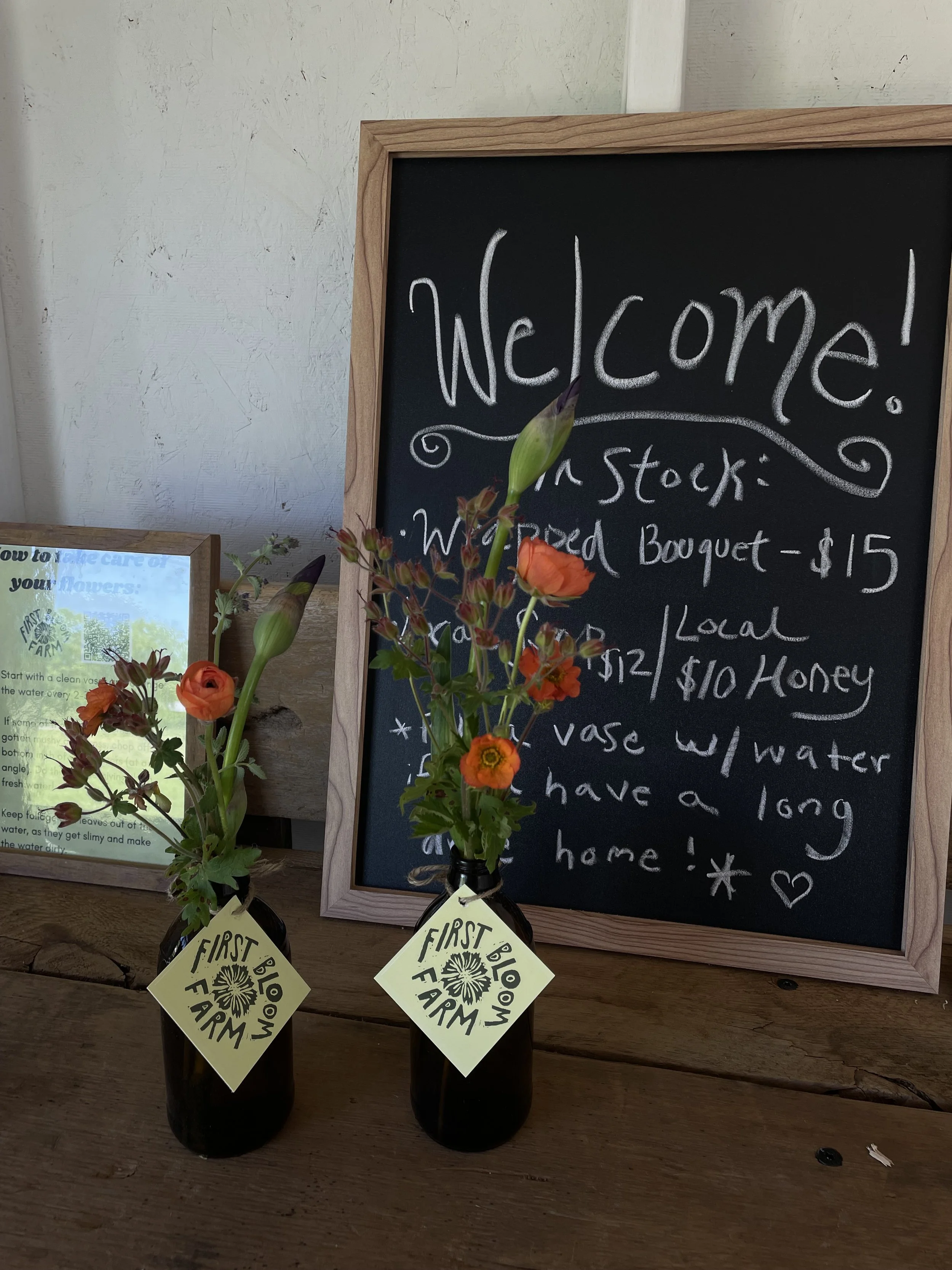 A chalkboard sign with shopping details and a flower arrangement in a small vase on a wooden table.