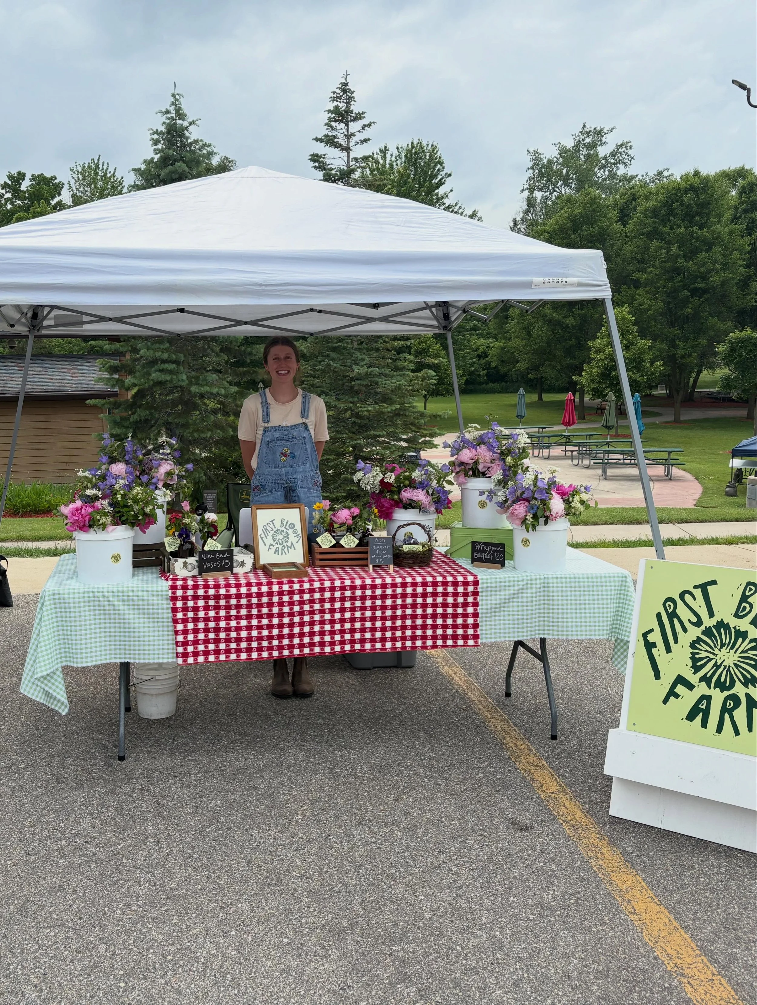 Morgan from First Bloom Farm at the Sparta Farmers Market under a white canopy.