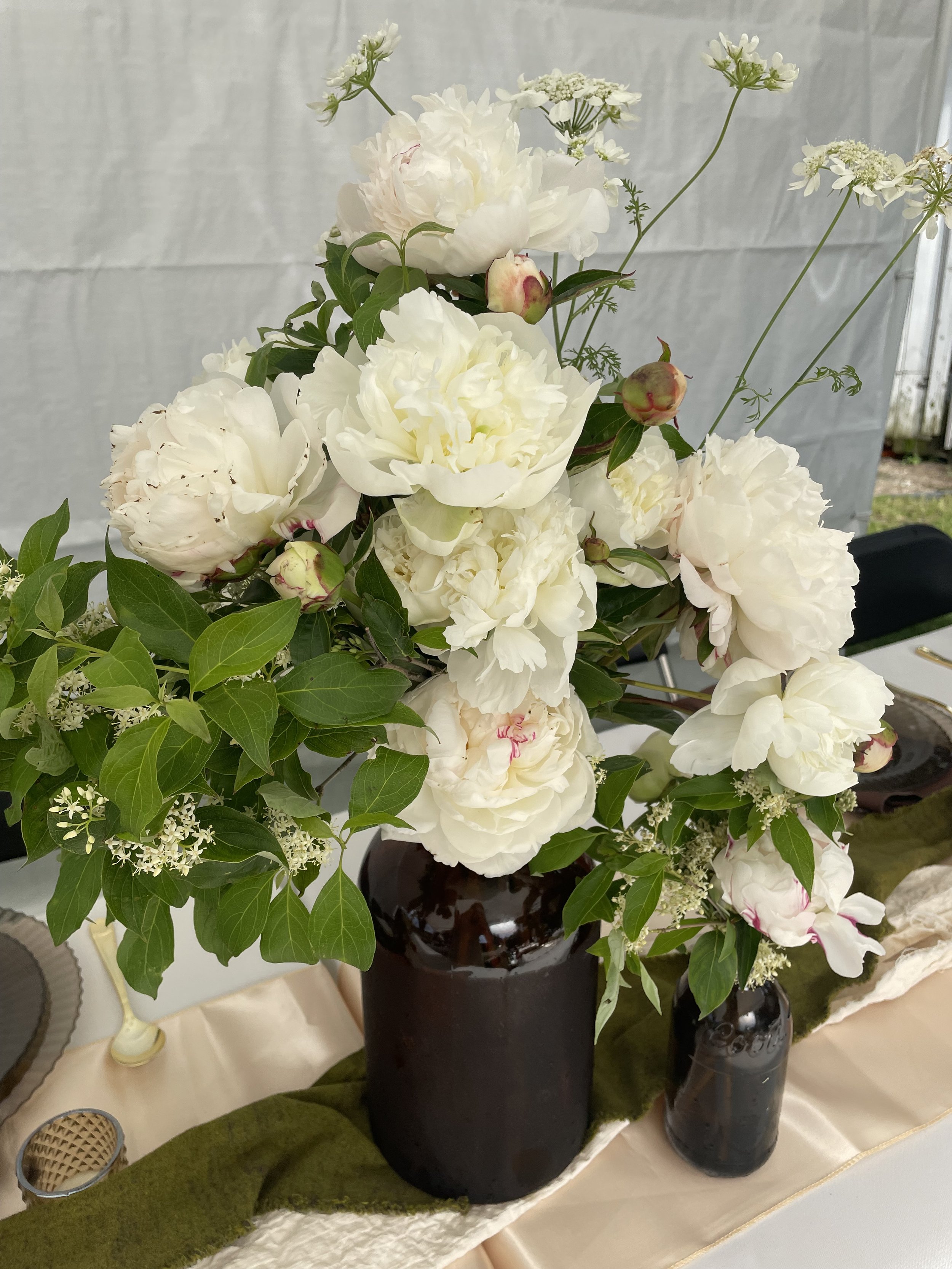 A floral arrangement with white peonies in a dark brown vase on a table.