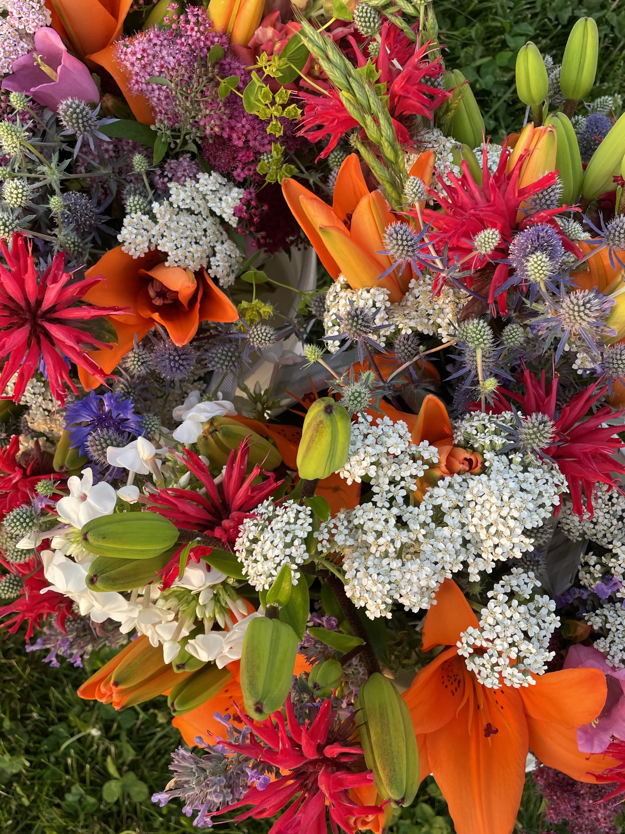 Close-up of a vibrant, colorful bouquet of various flowers, including orange, red, pink, white, and purple blossoms, and green foliage.