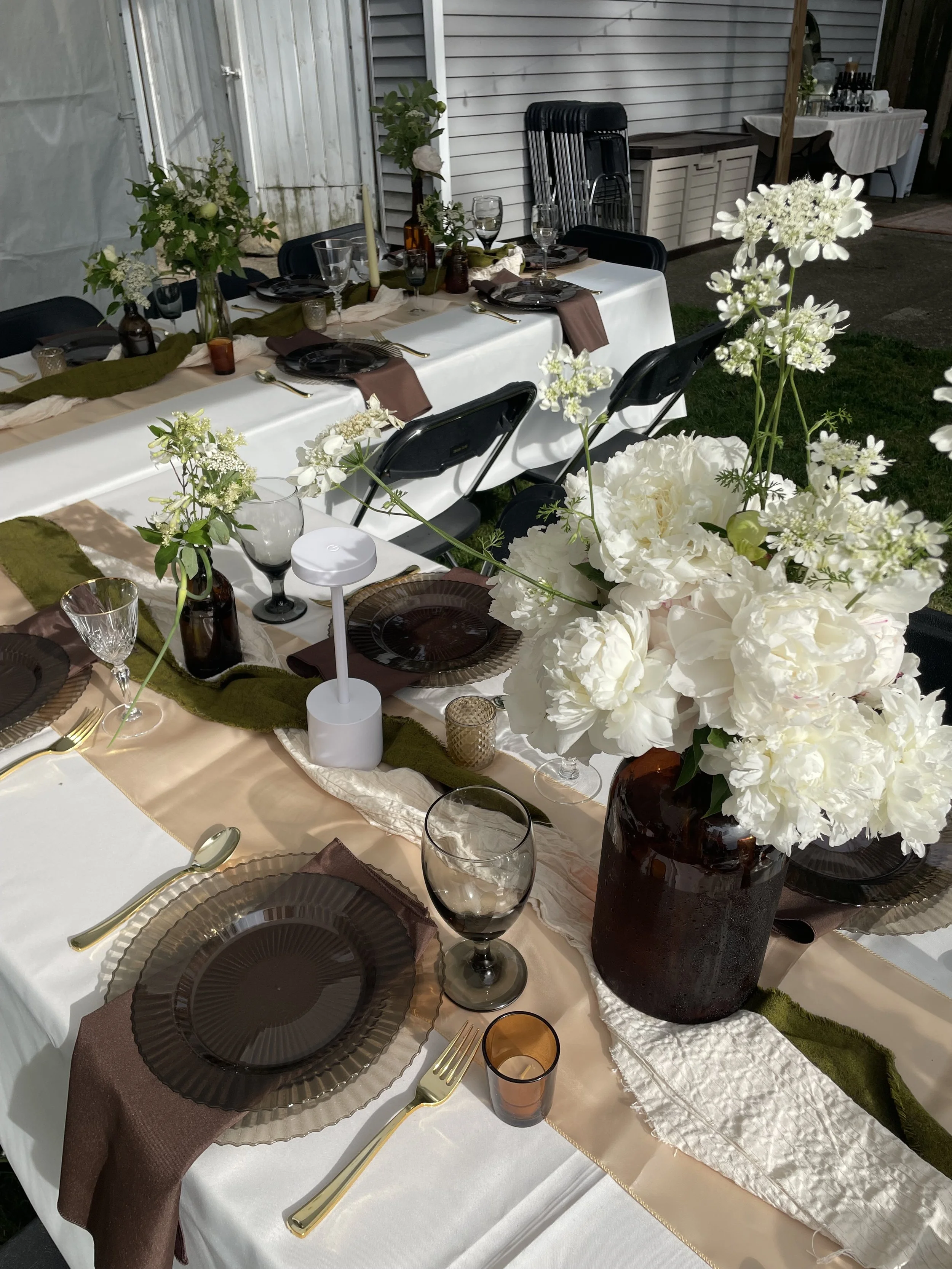 Custom floral centerpieces, candles, glassware, and dark plates with gold utensils set up for an event.