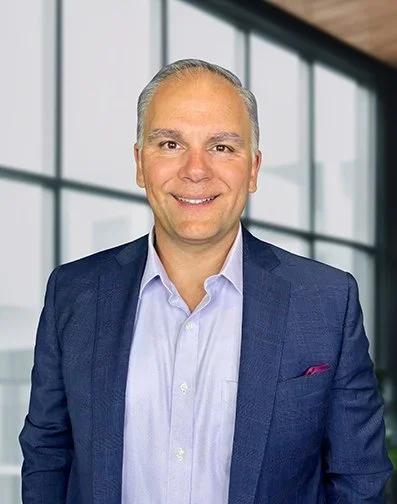 Professional man smiling in an office with large windows.