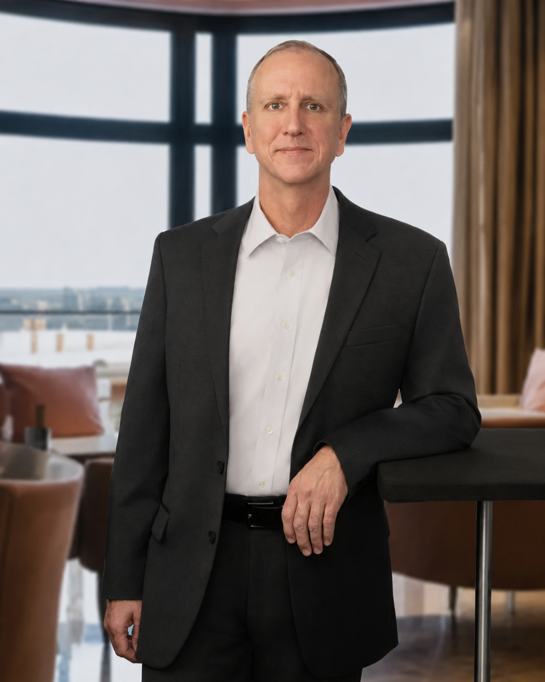 A middle-aged man in a black suit and white dress shirt standing in a modern room with large windows and curtains.