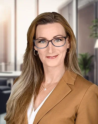 Professional woman with long hair, glasses, and earrings, wearing a brown blazer, in an office setting.