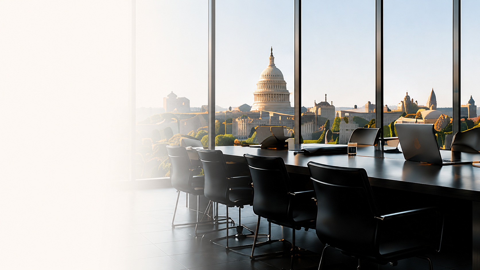 A modern office conference room with a large window overlooking the US Capitol building, with chairs and laptops on the table.