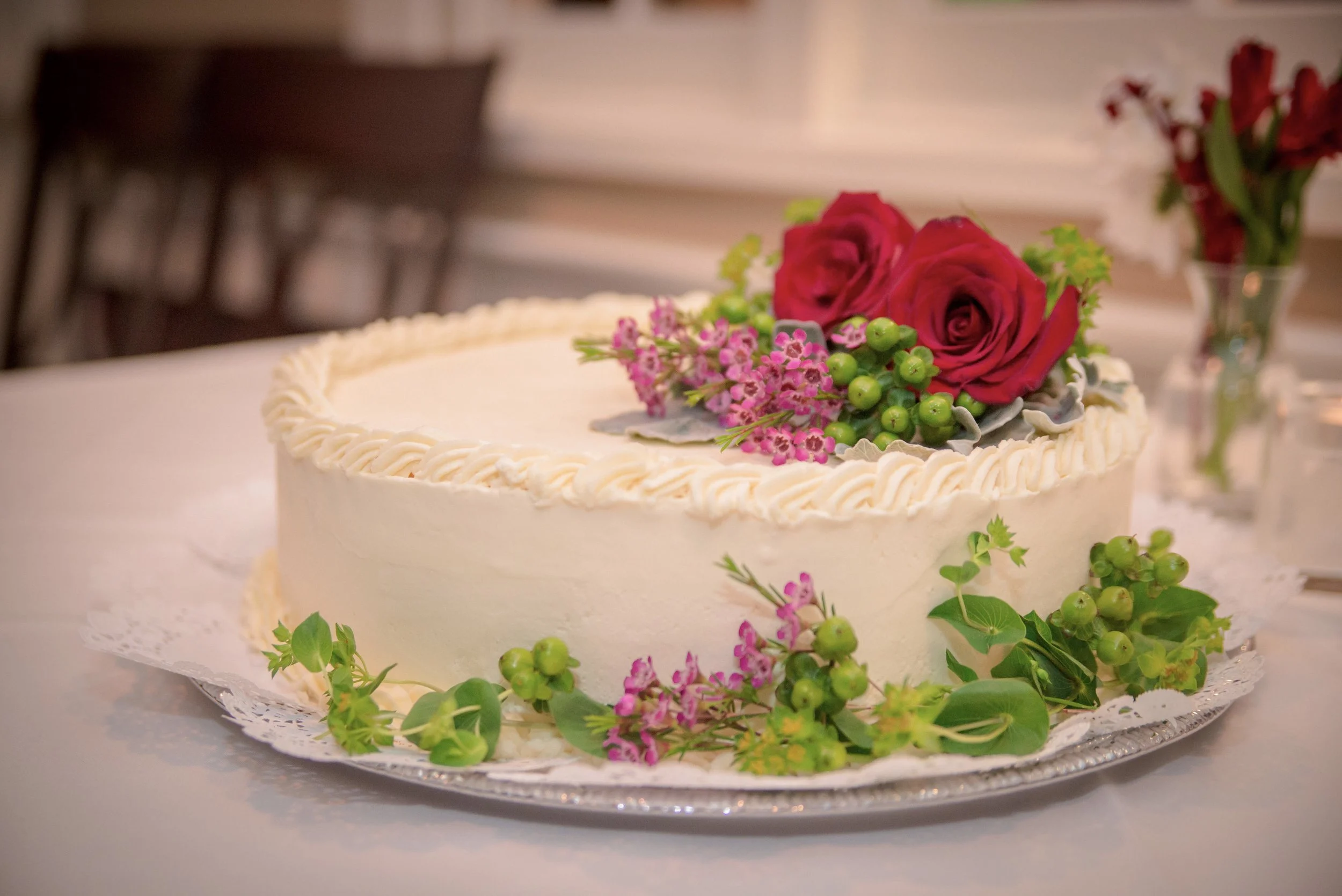 A white wedding cake decorated with red roses and greenery.