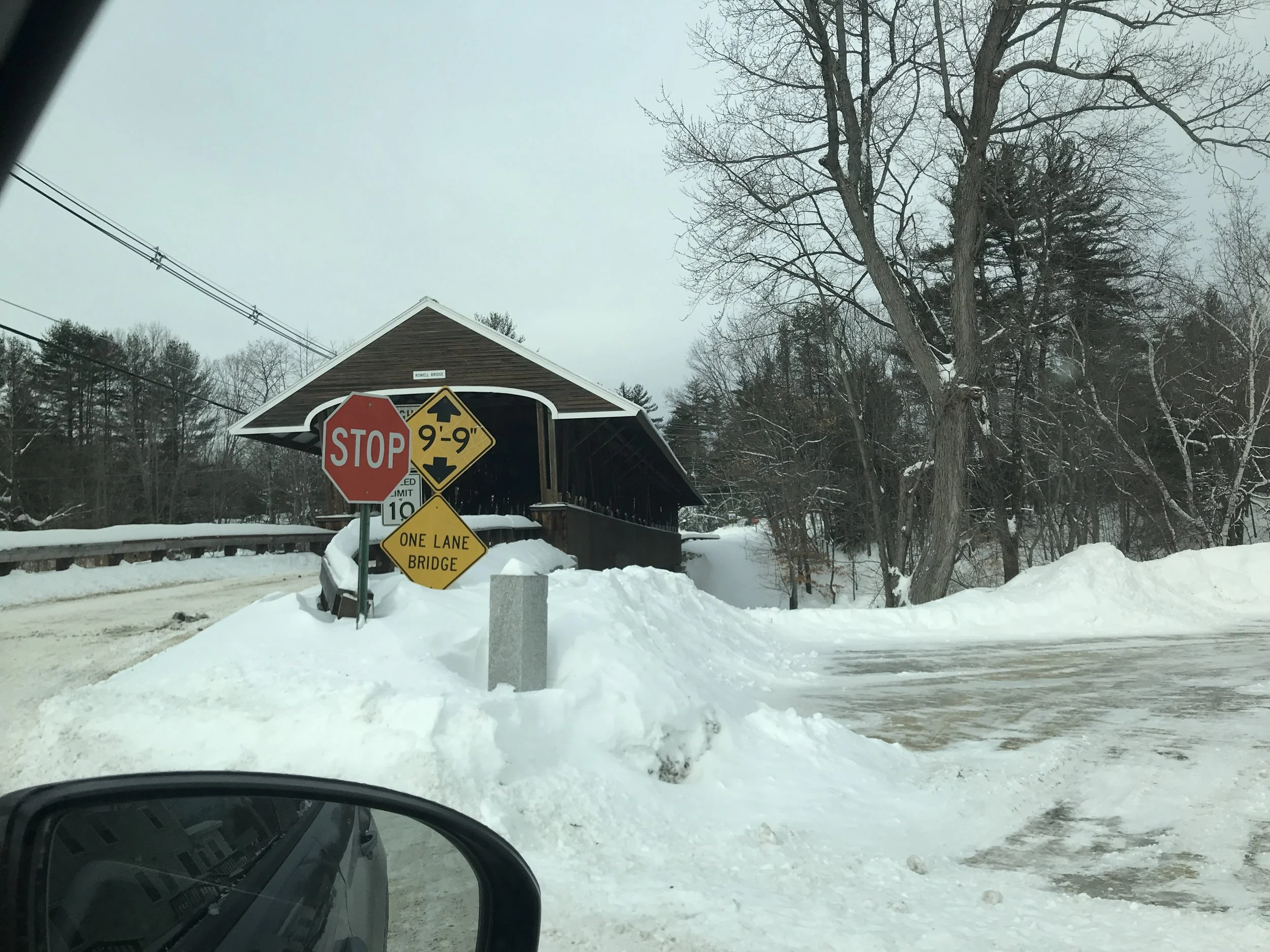 A red covered bridge in the snow with a one-lane bridge sign.