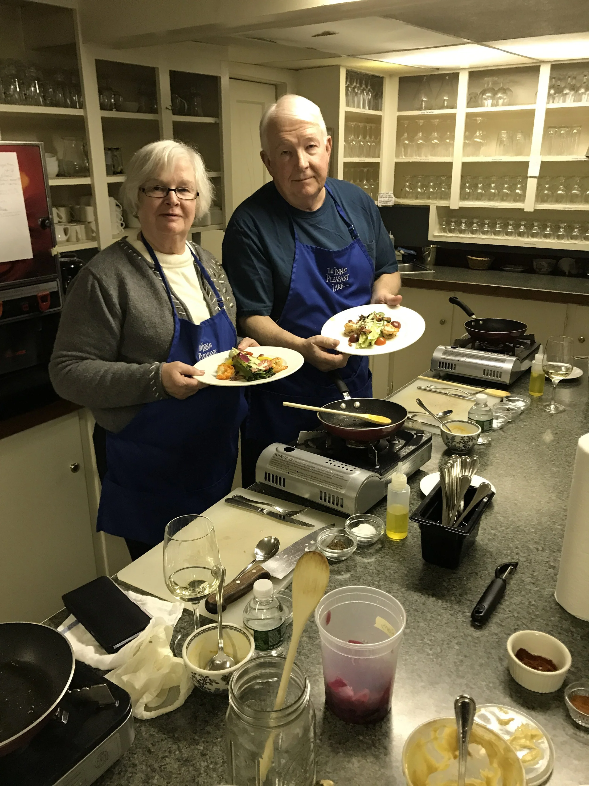Two people in blue Inn at Pleasant Lake aprons holding finished plated dishes in the kitchen.