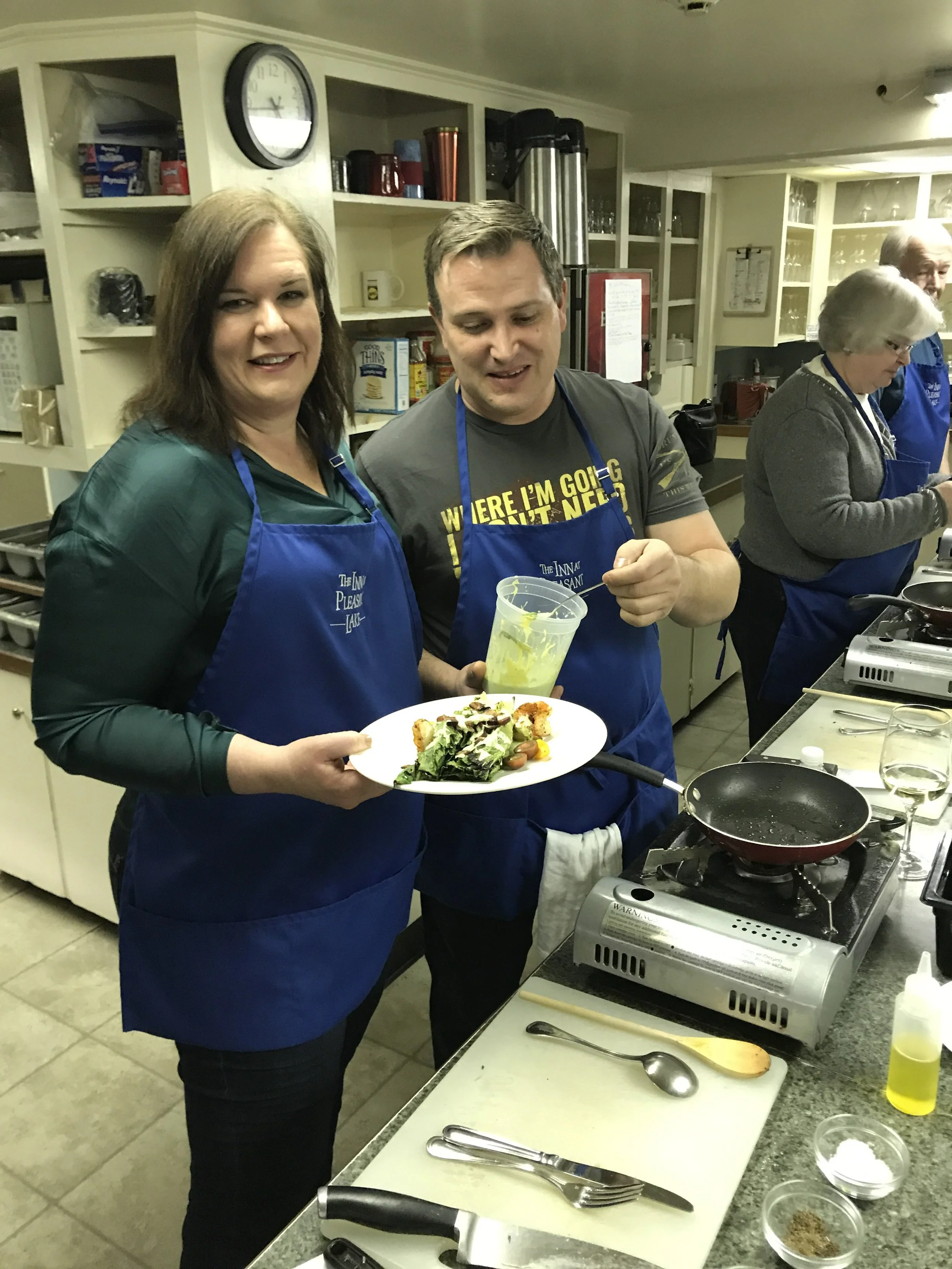 A couple in blue inn aprons presenting a plated salad at a cooking station.