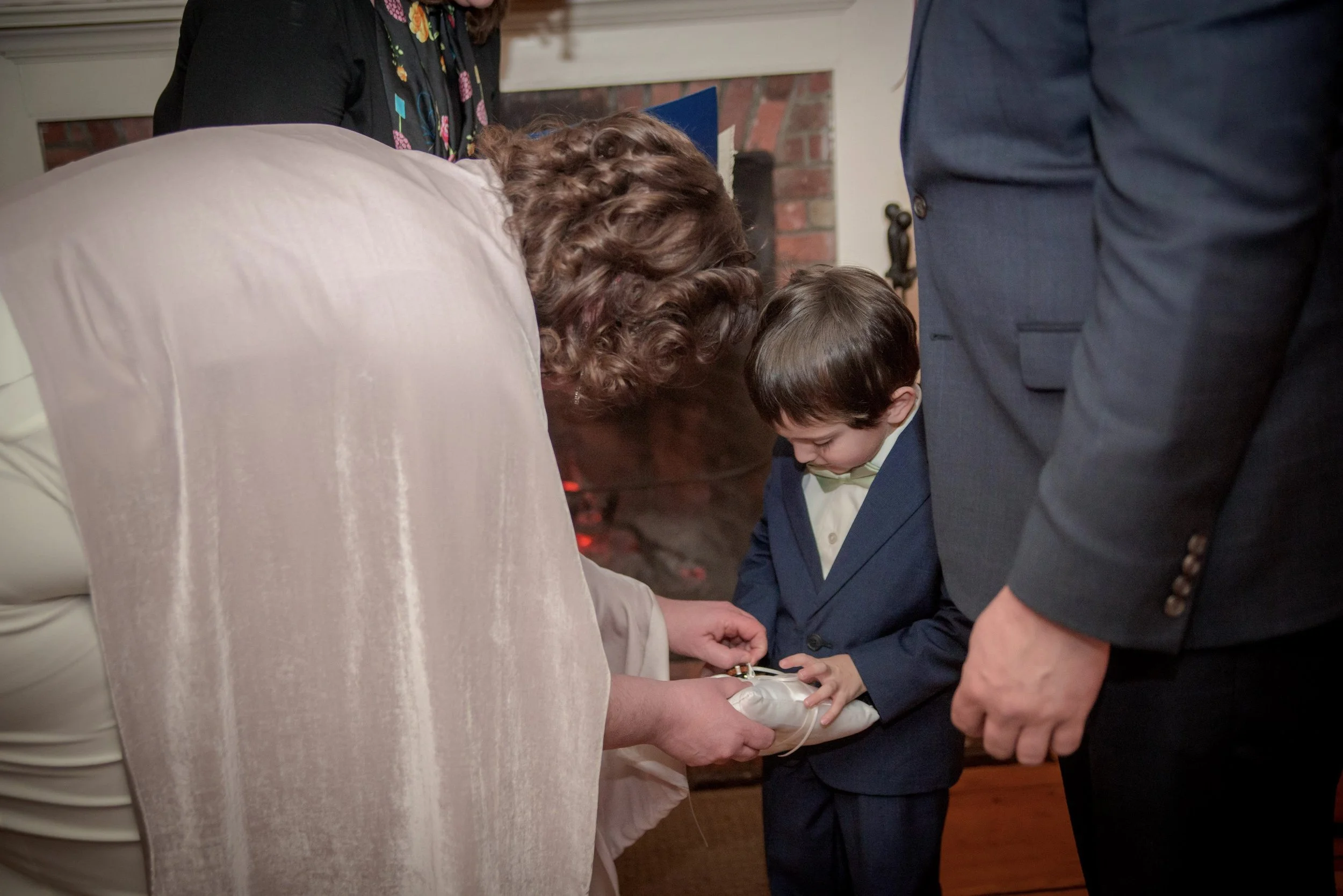A woman in a pink dress adjusting the young ring bearer's pillow.