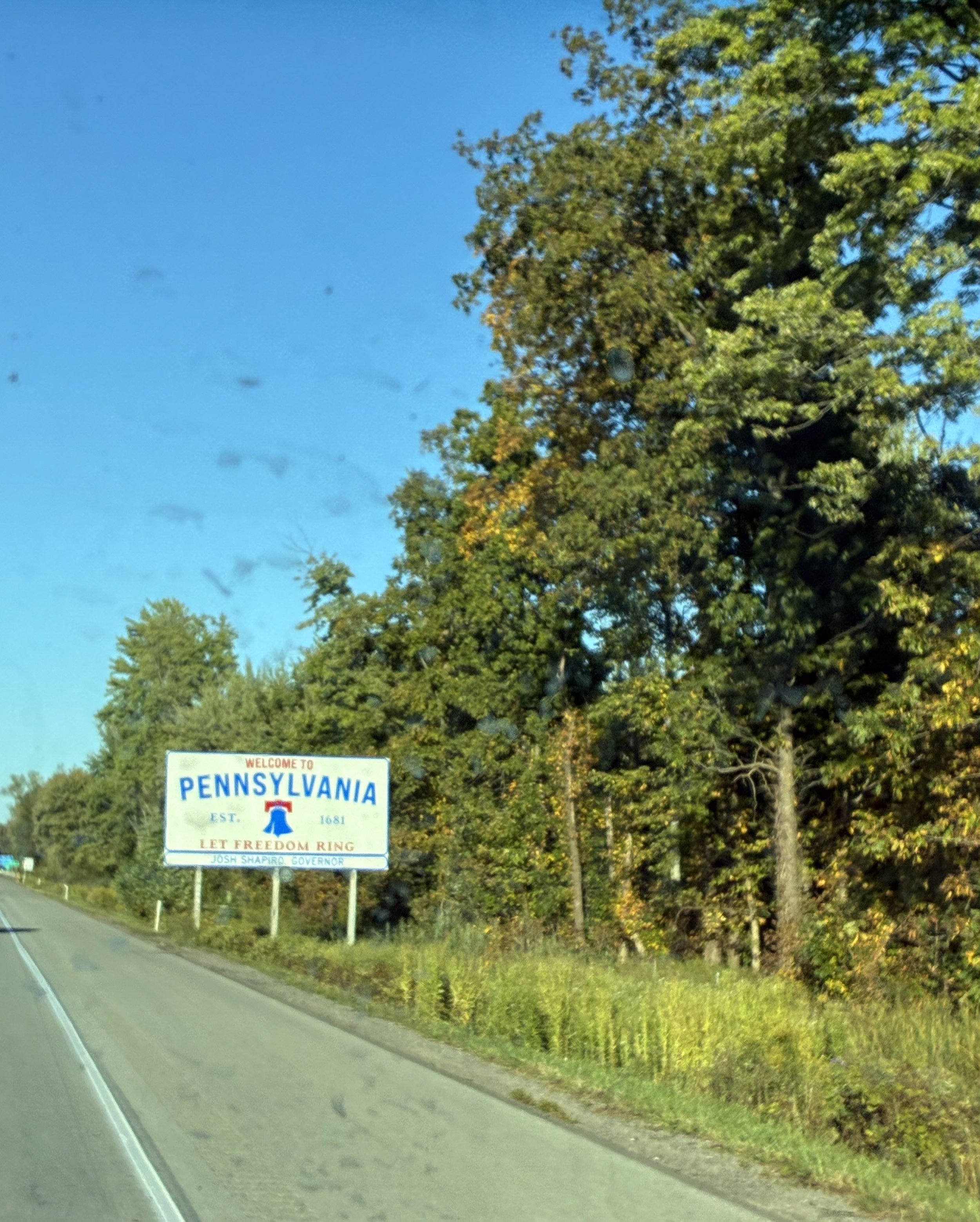 A Welcome to Pennsylvania roadside sign with early-fall trees.