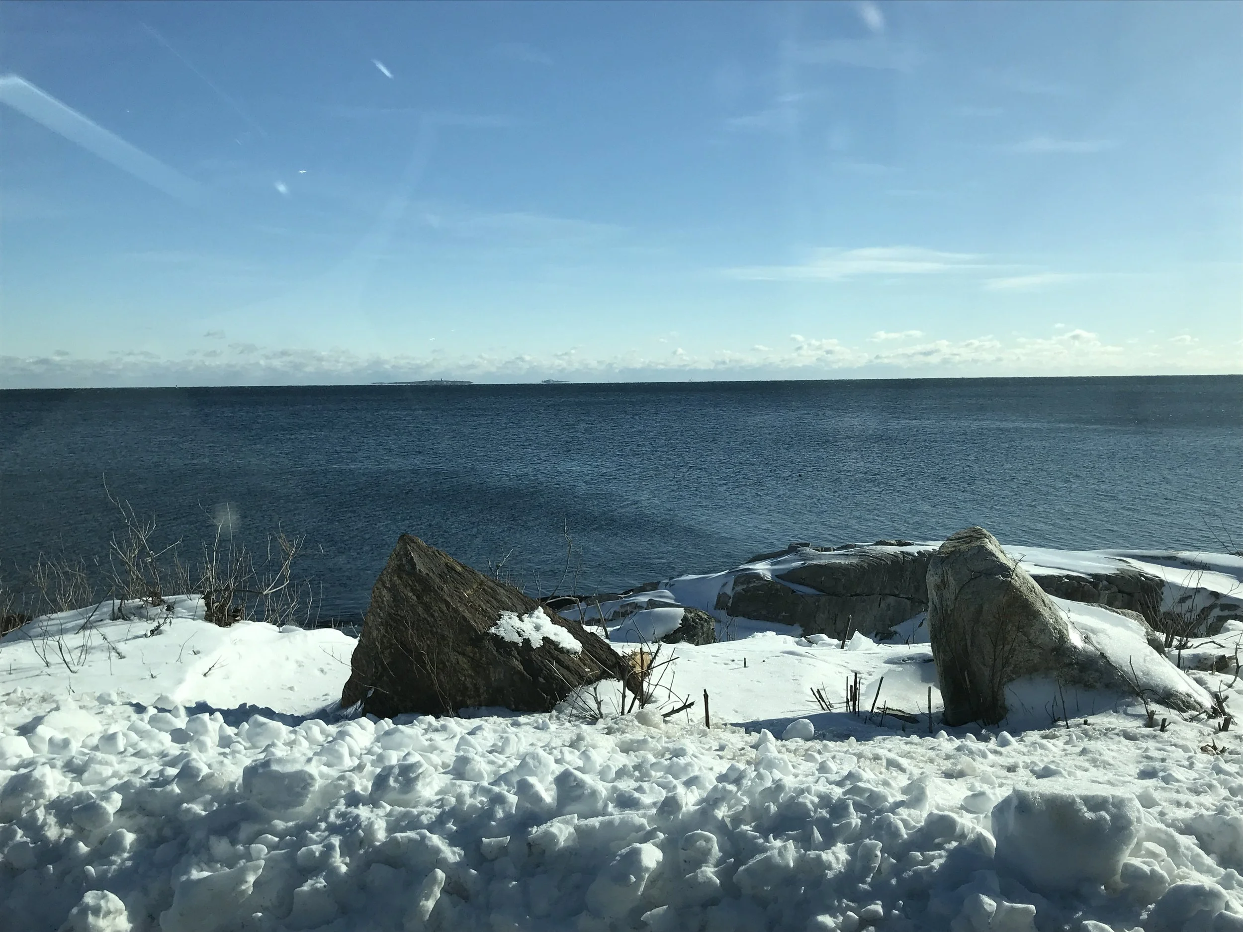 A snowy ocean shoreline with rocks and waves.