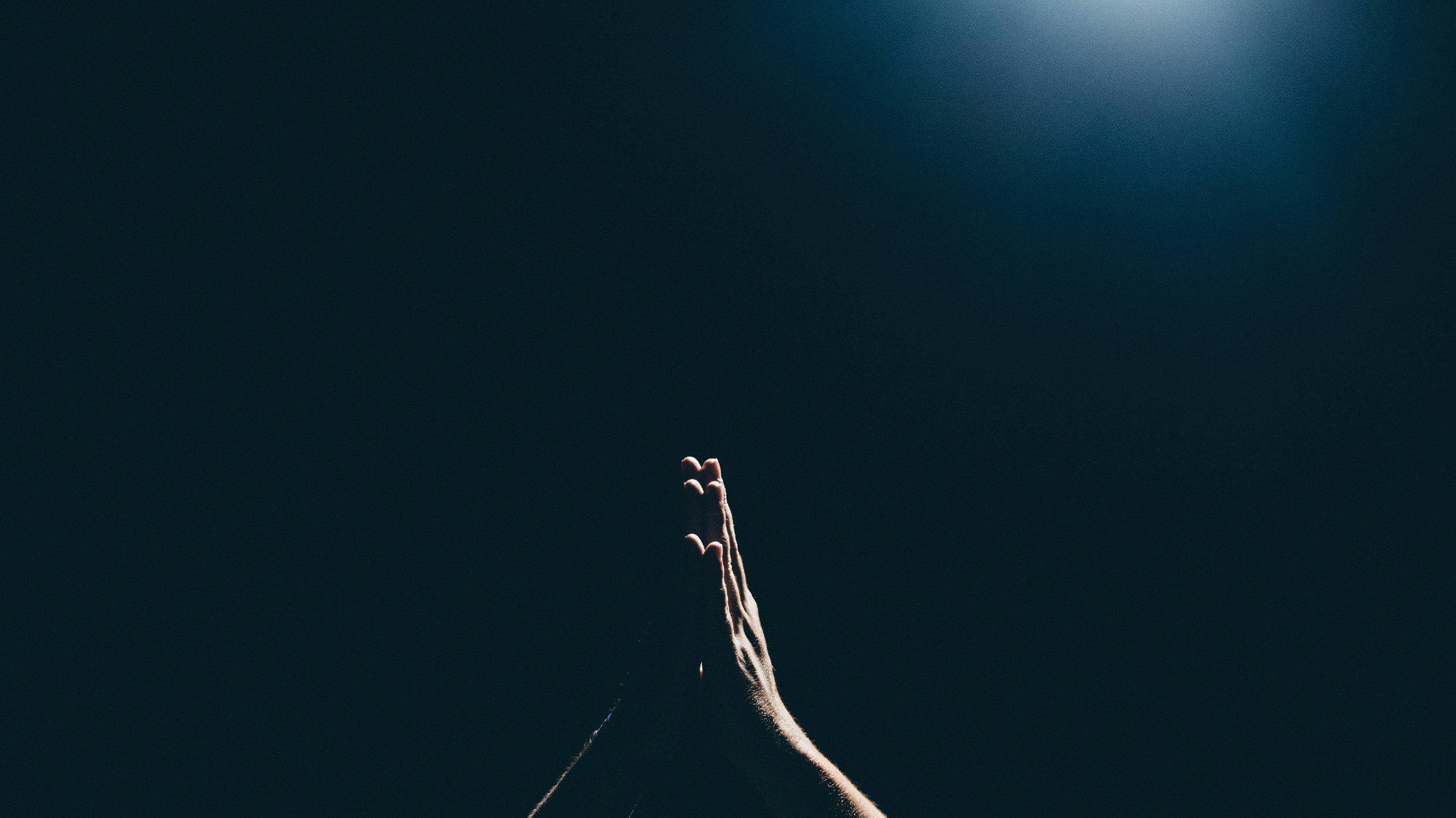 A hand reaching up towards a bright light in a dark room.