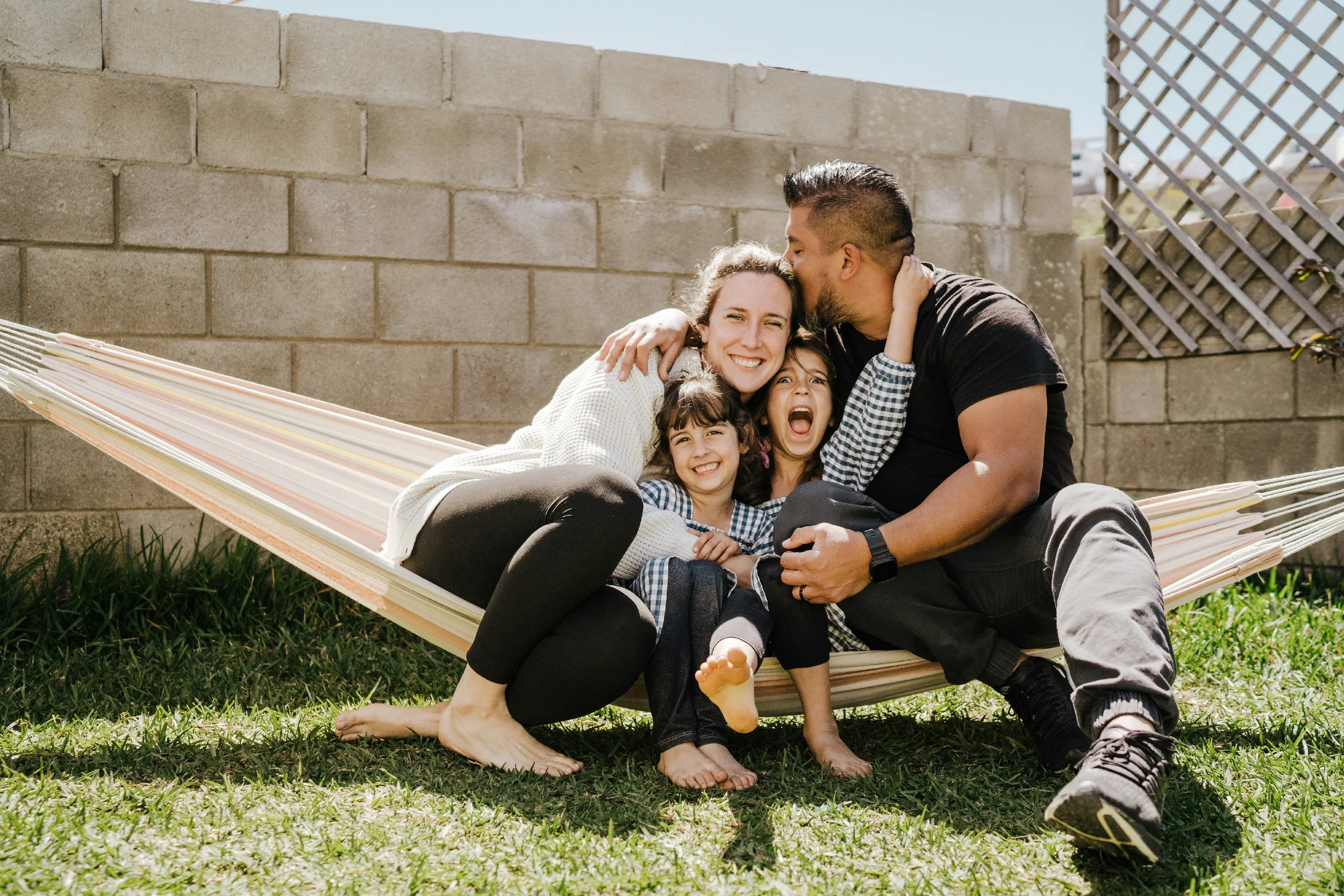 A family sitting on a couch enjoying a moment together. A man playing guitar, a young girl reaching towards him, and a woman smiling at the girl.
