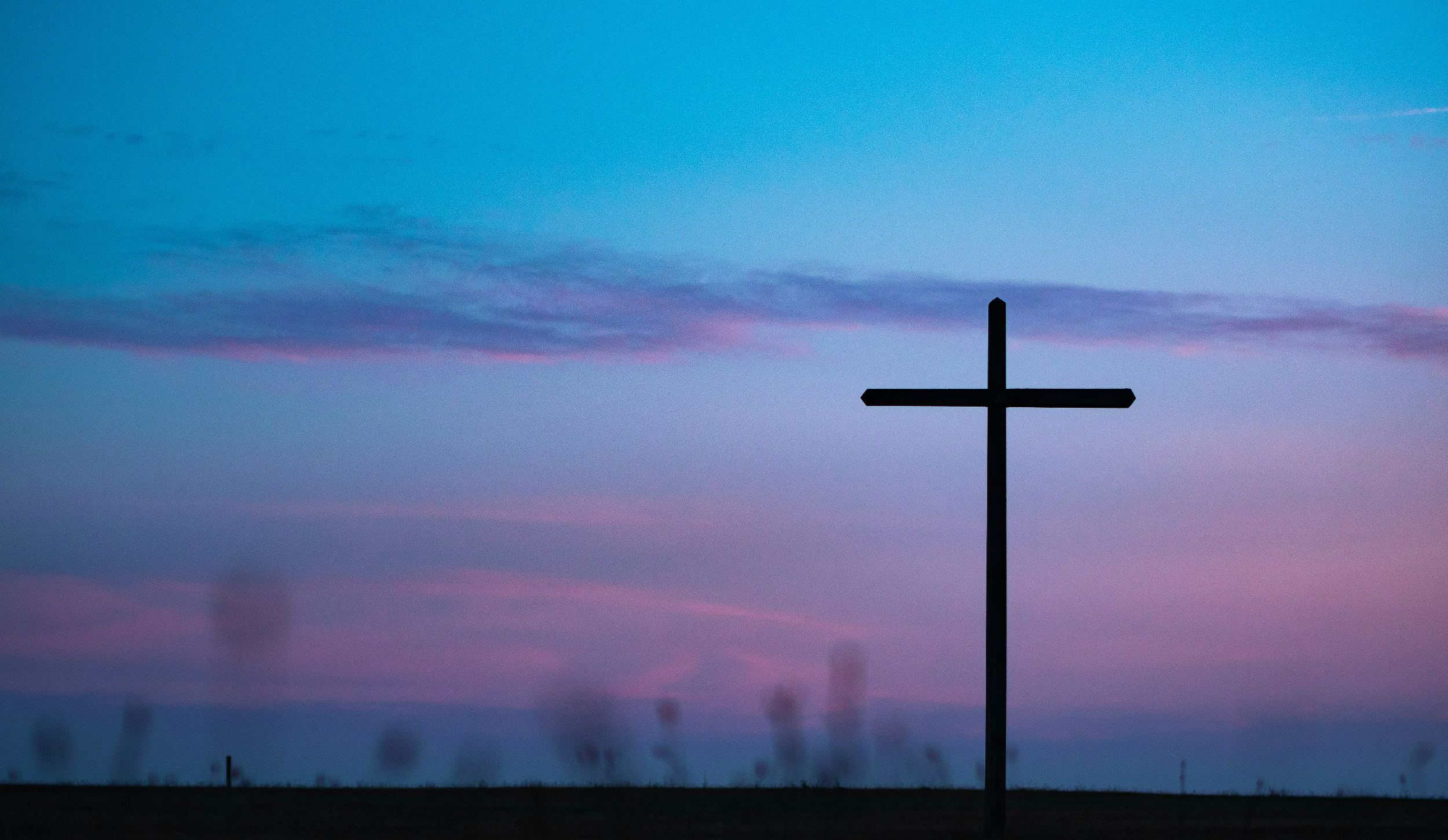 A silhouette of a cross against a colorful twilight sky with purple and blue clouds.