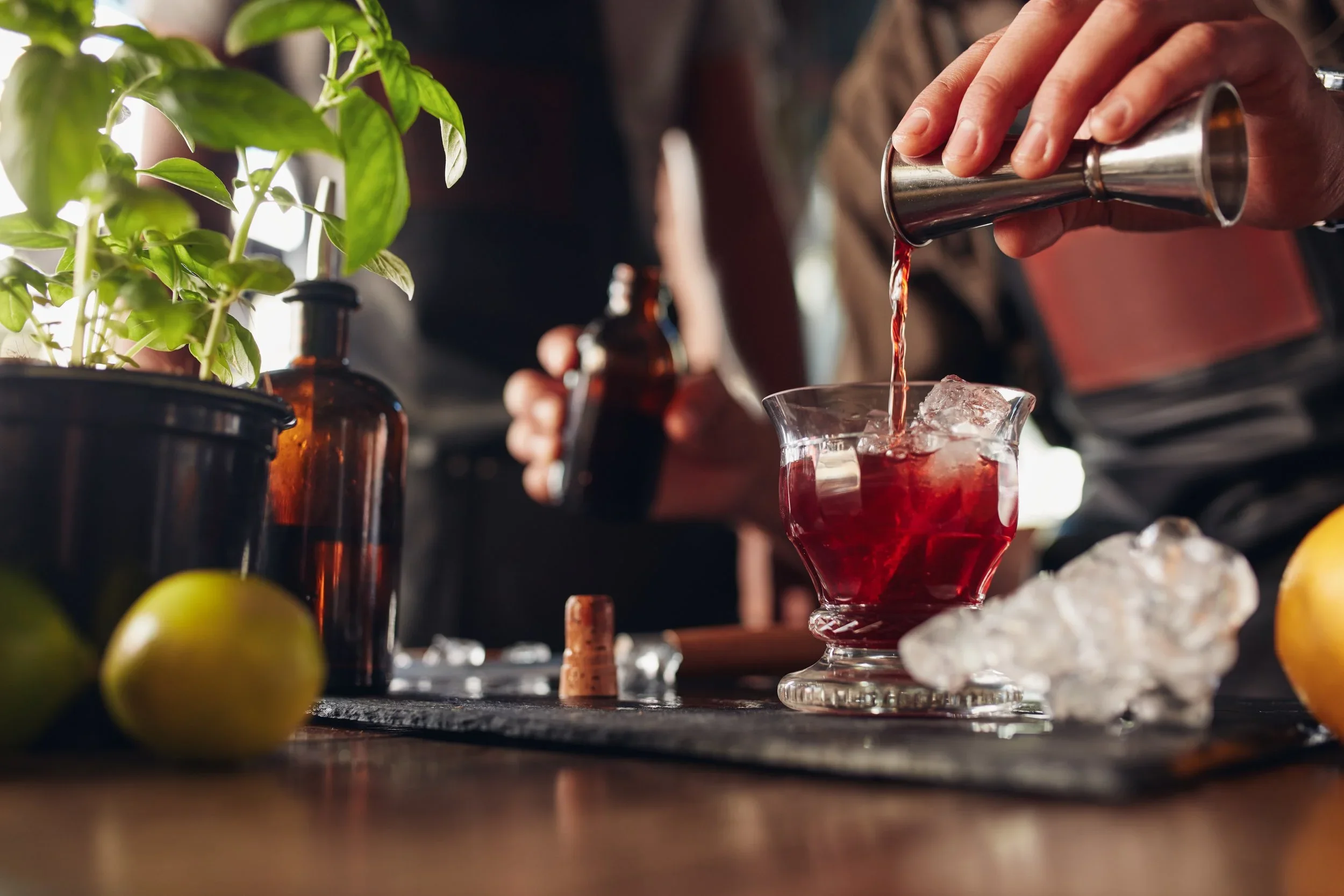 A cinematic photo of a bar tender pouring a red liquid into a cocktail glass on a bar.