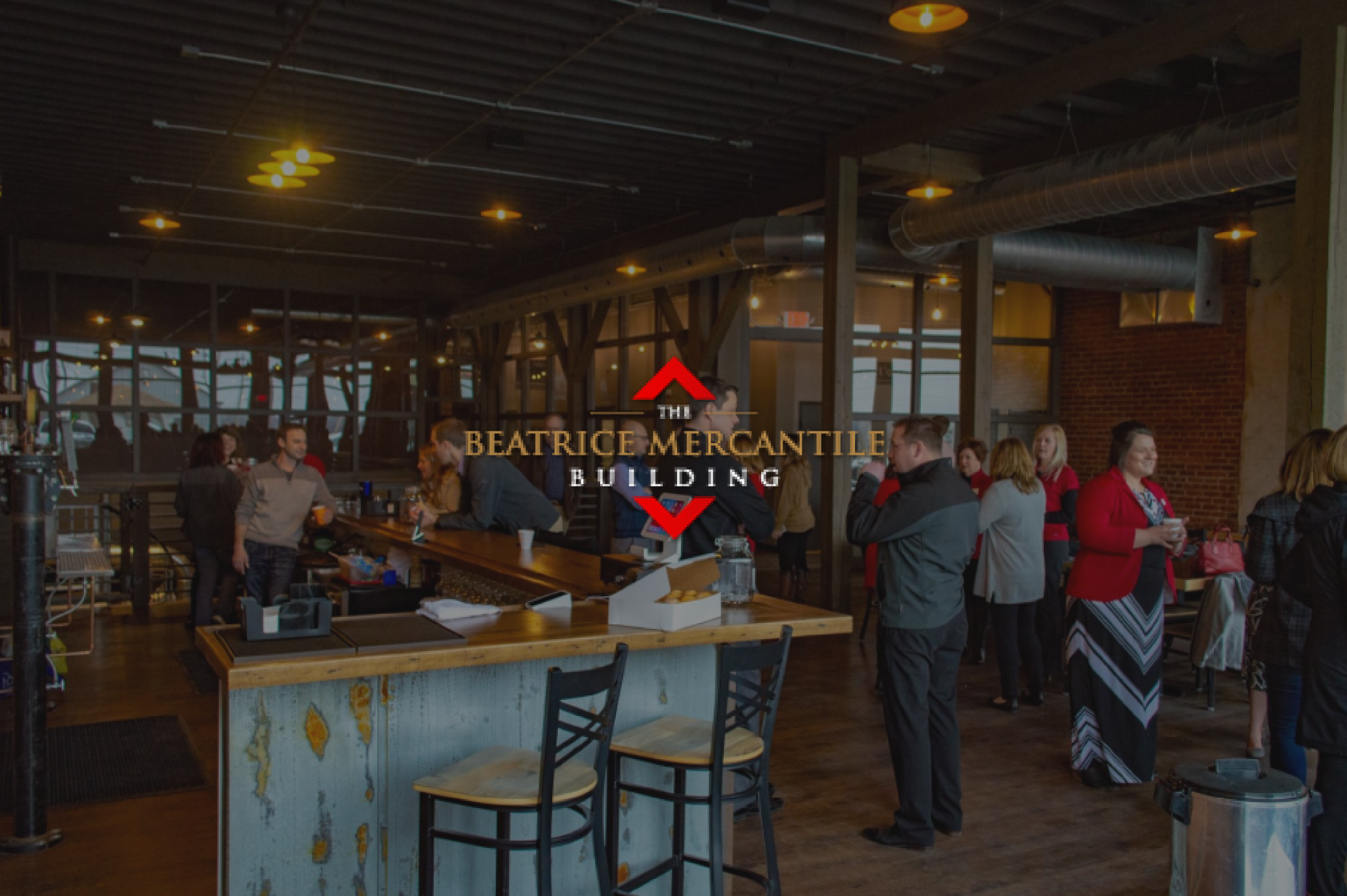 A photo of the warm, rustic interior of Stone Hollow Brewery inside the building, with the red and gold Beatrice Mercantile logo overlaid in the center.
