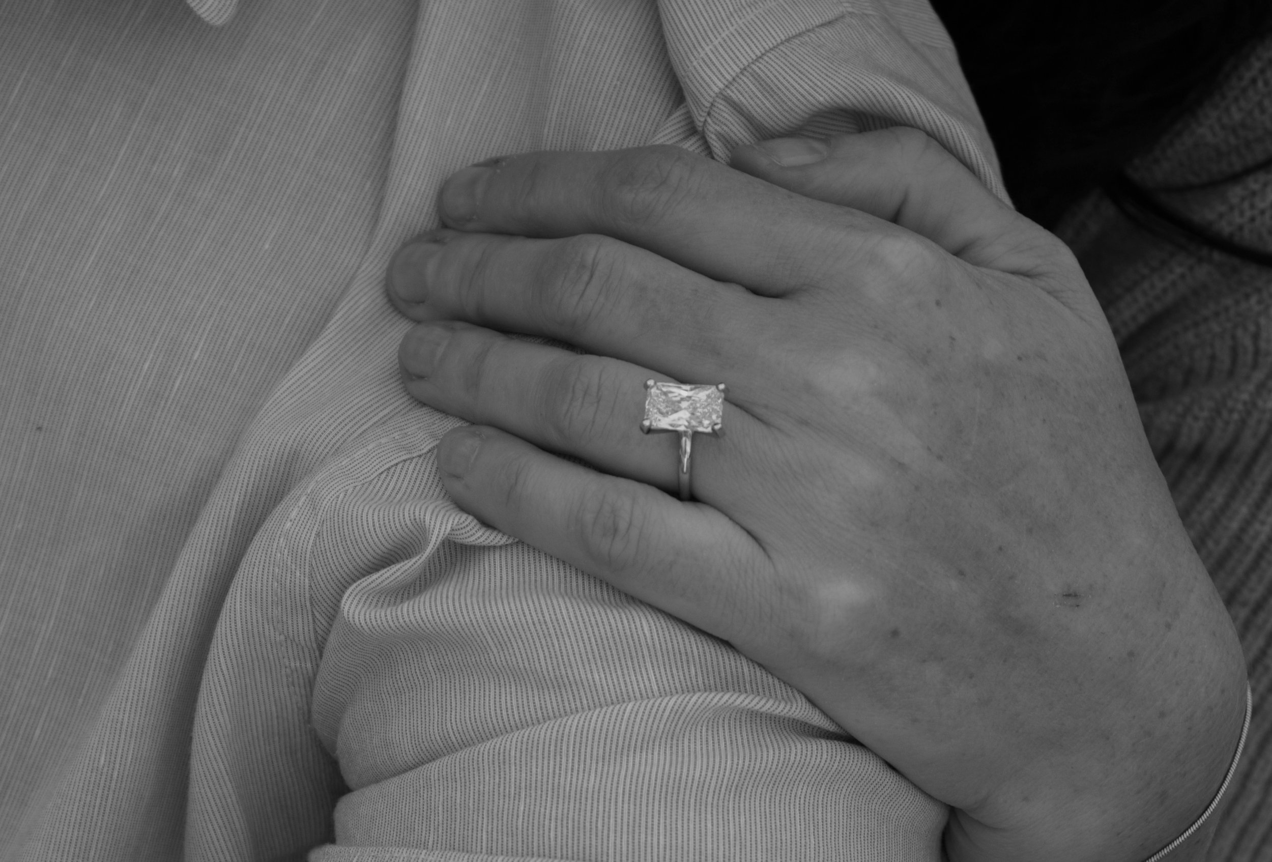 Close-up of a person's hand resting on another person's arm, with a large diamond engagement ring on their finger.