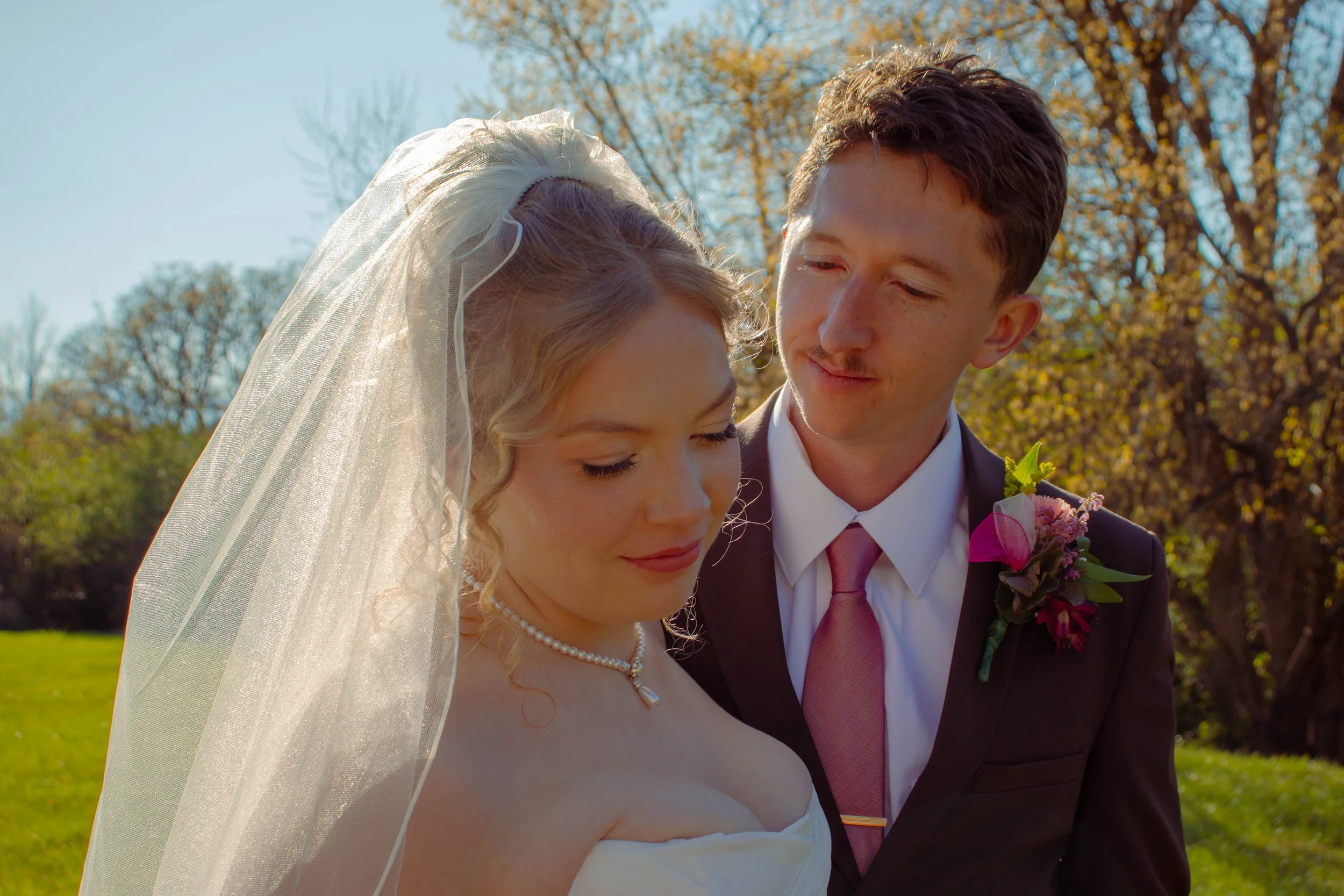 A bride and groom standing outdoors under a tree with autumn leaves, gazing at each other during their wedding ceremony.