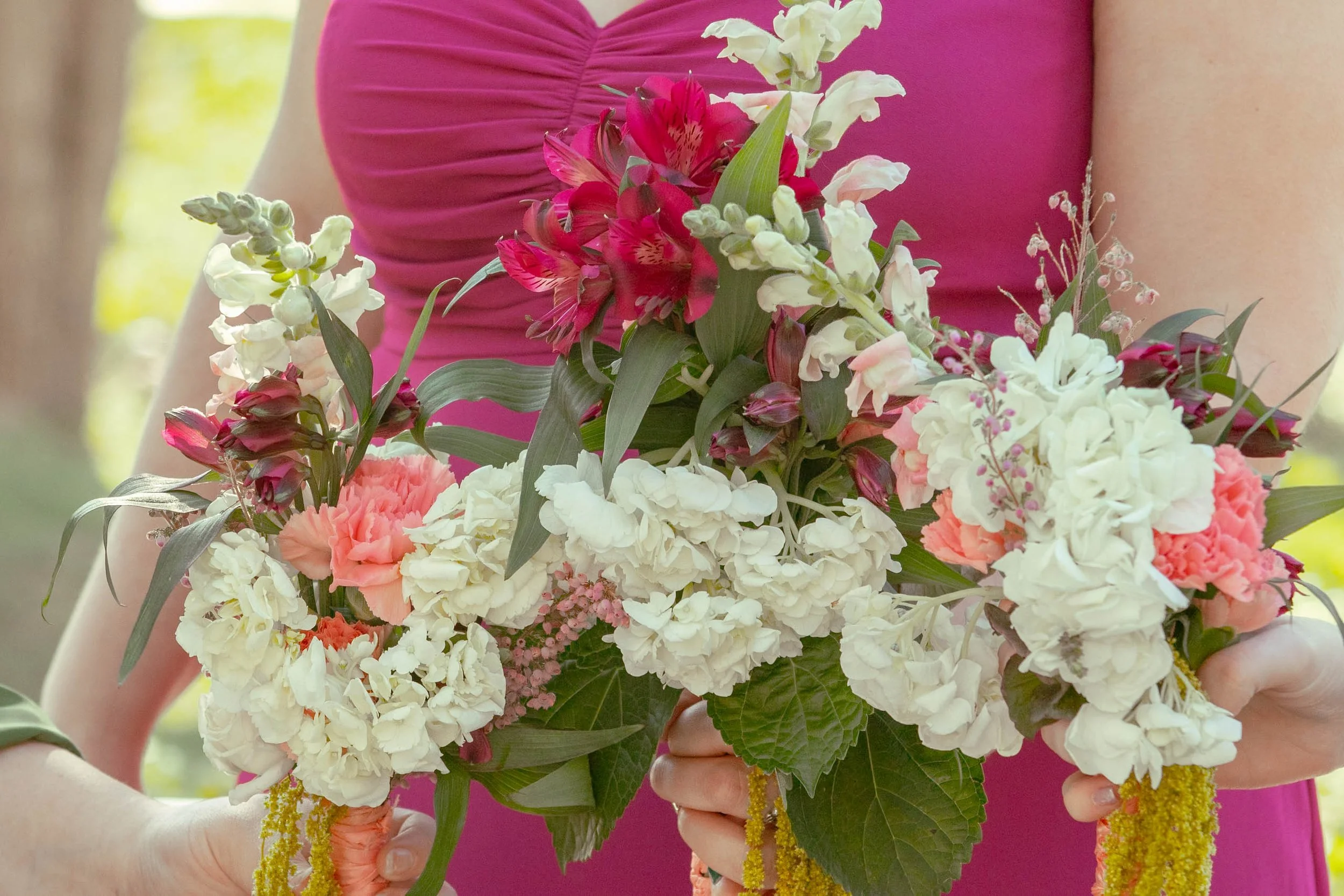 Person in a pink top holding a bouquet of various pink, white, and cream flowers including hydrangeas and lilies.