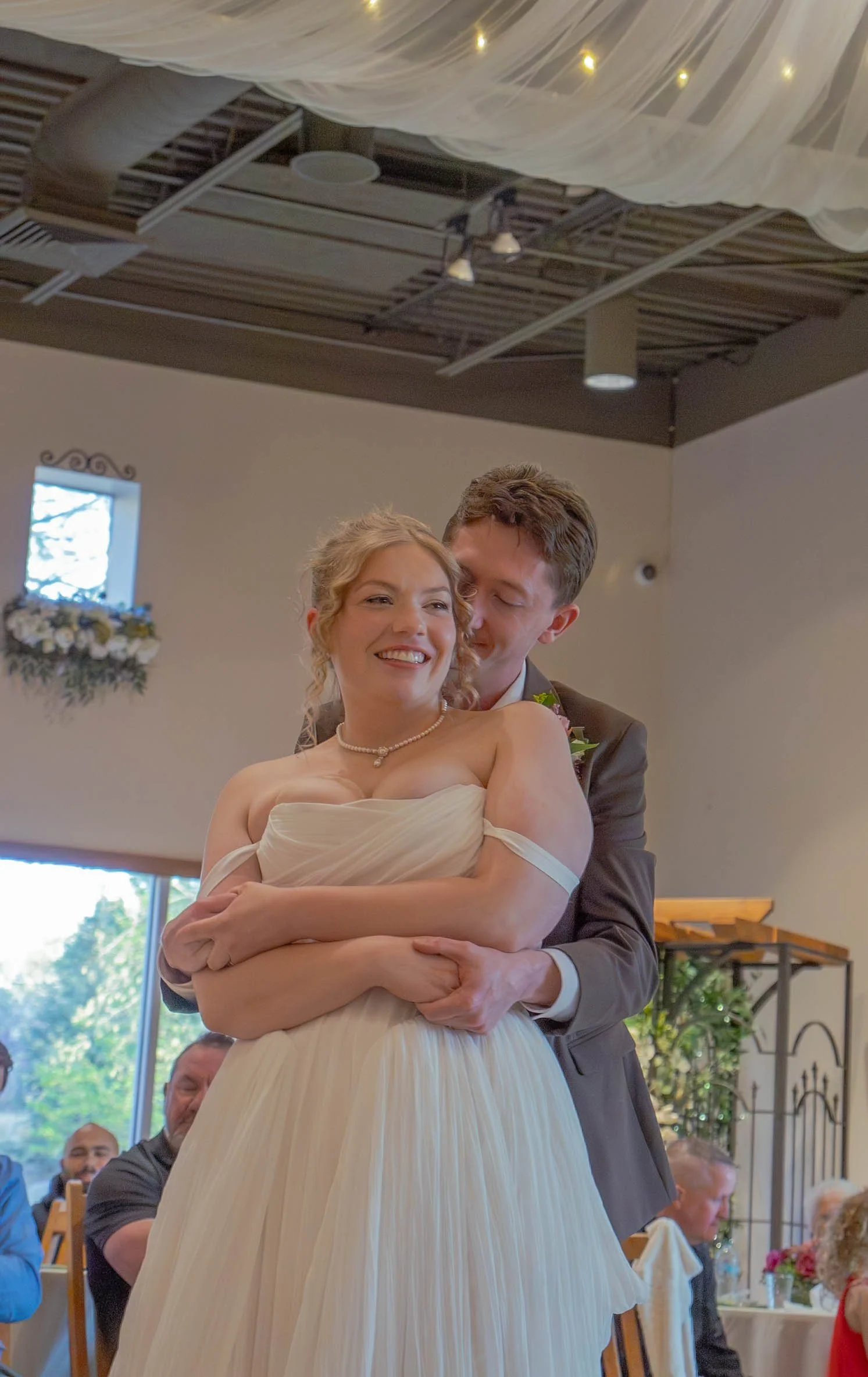 A bride and groom sharing a dance at their wedding reception, smiling and embracing each other in a decorated indoor venue.