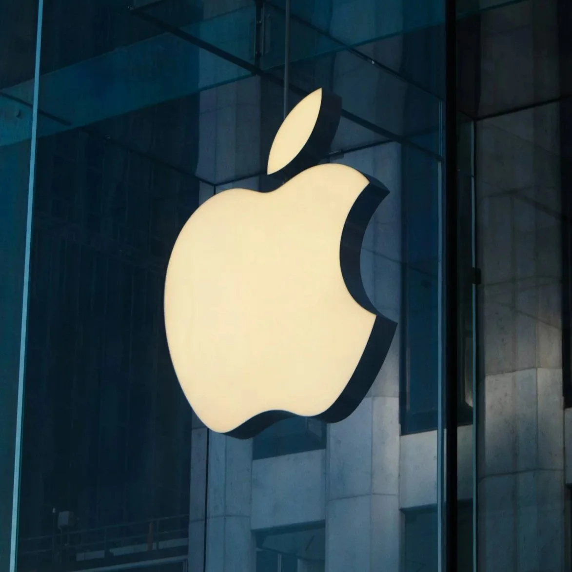 Illuminated white Apple logo on a building exterior at night.