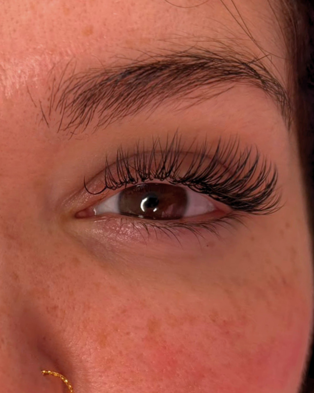 1:1 classic lash extensions, close up of brown eye, freckled face, looking directly forward.